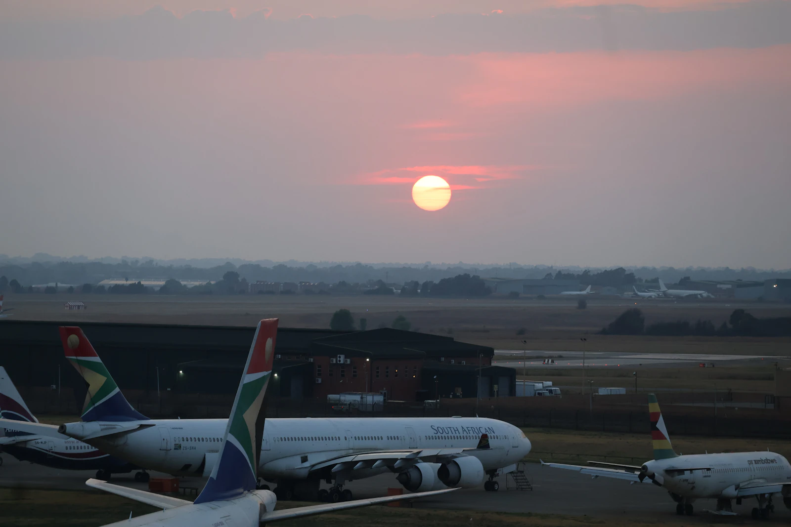 Passenger airliners parked on an airport tarmac at sunrise with a warm golden glow across the apron