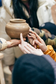 Hands passing a handmade clay pot