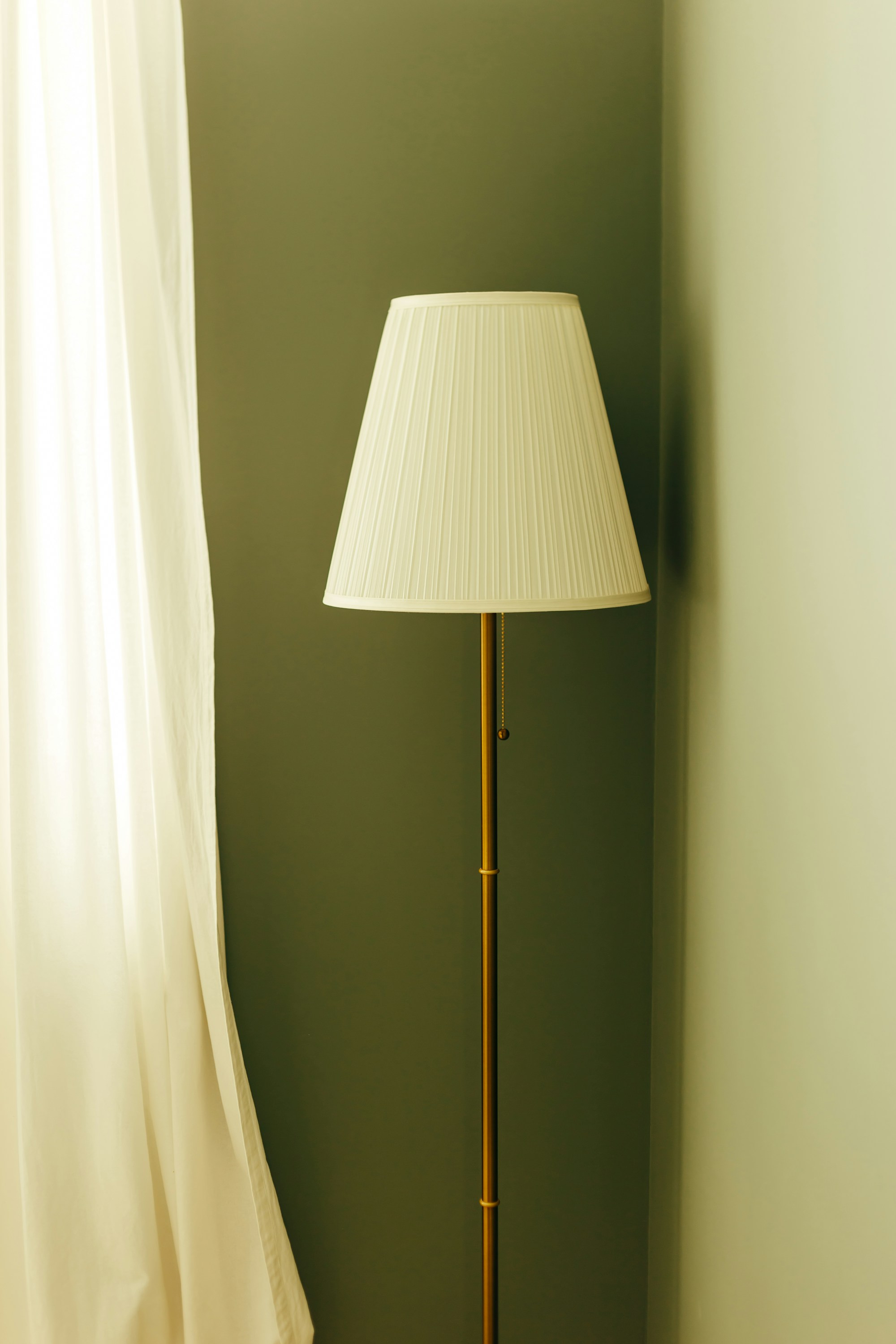 Tall floor lamp with a white shade standing in a bright room