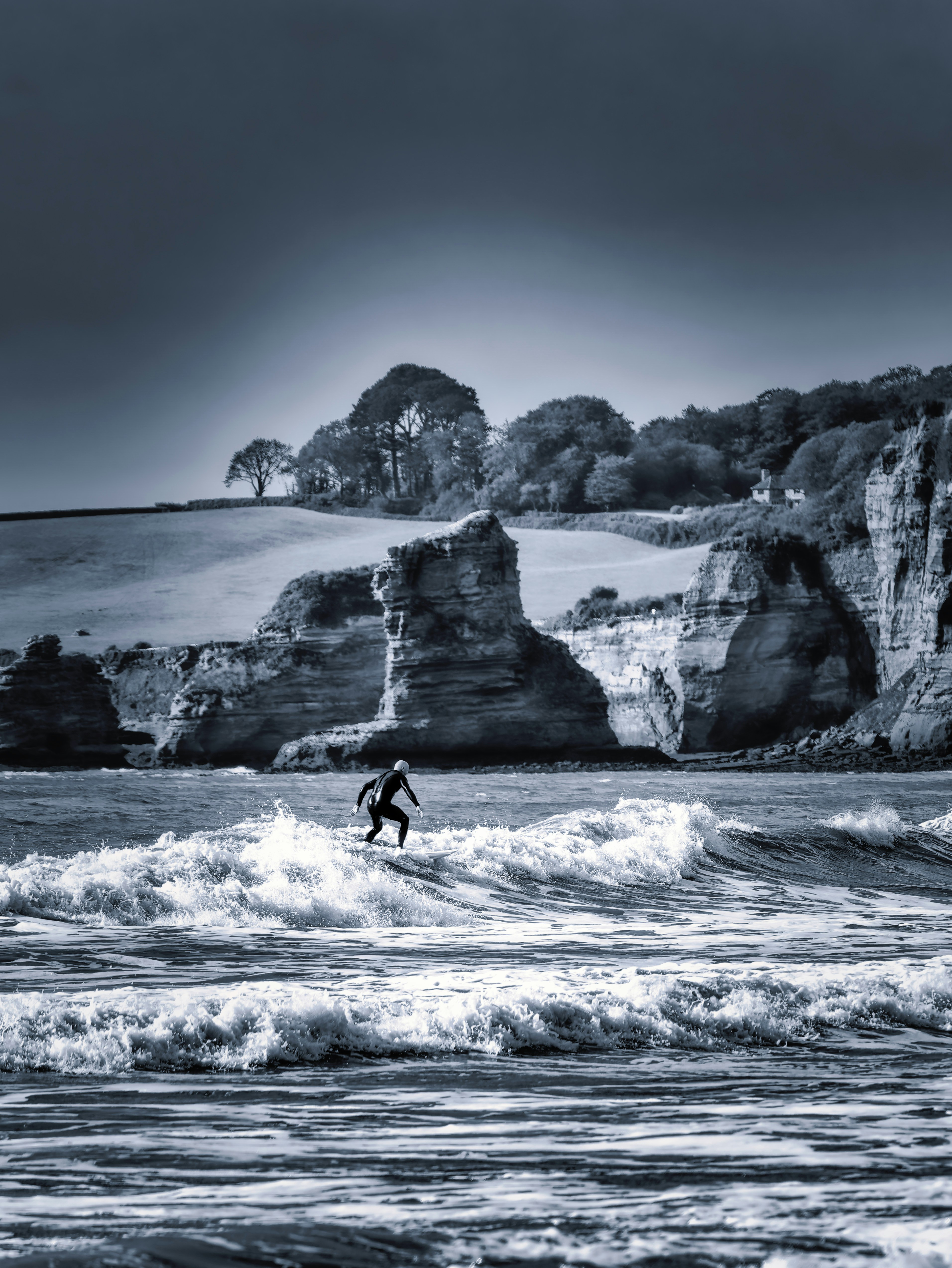 Surfer rides wave near dramatic coastal cliffs