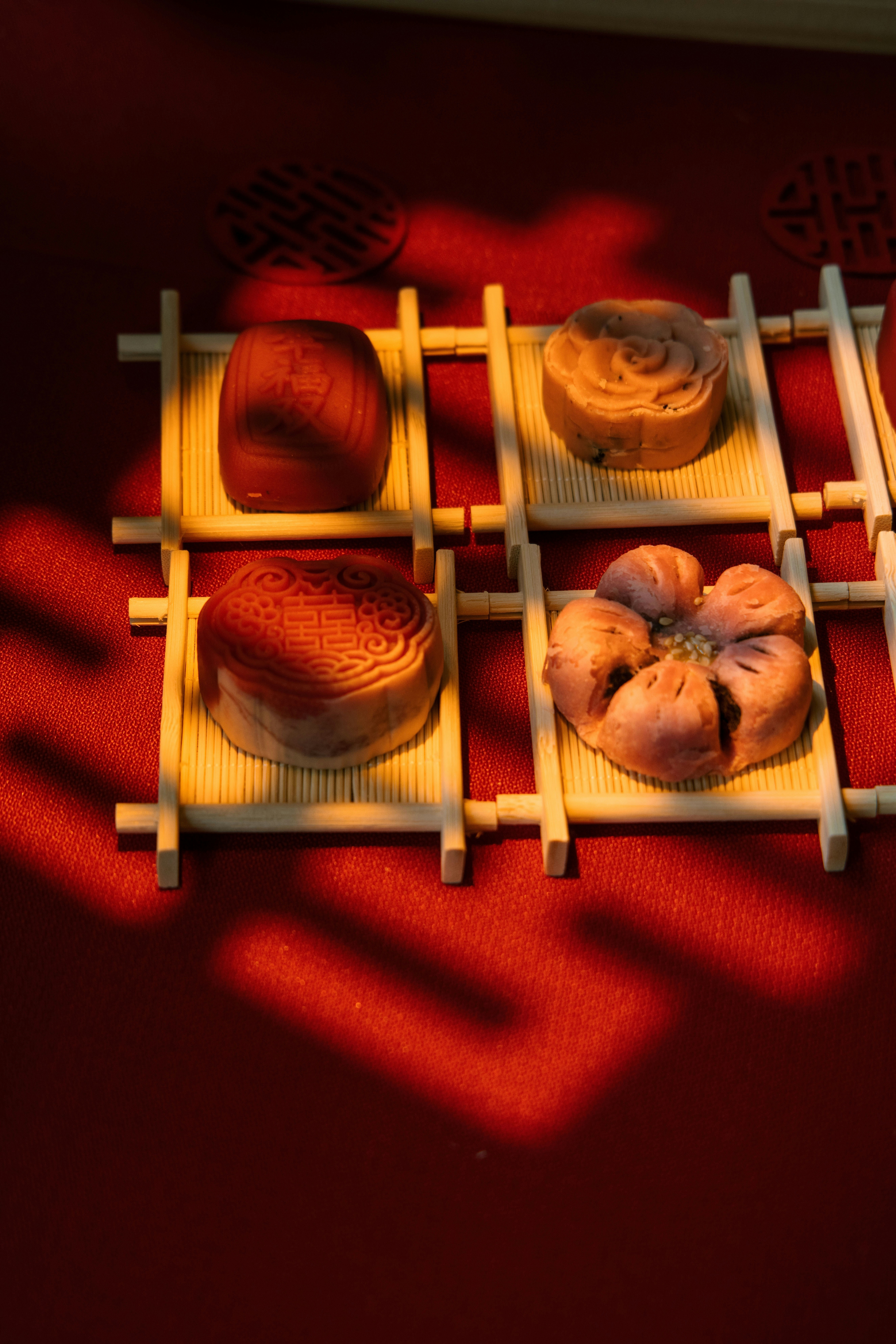 Four mooncakes arranged on bamboo mats on red background.