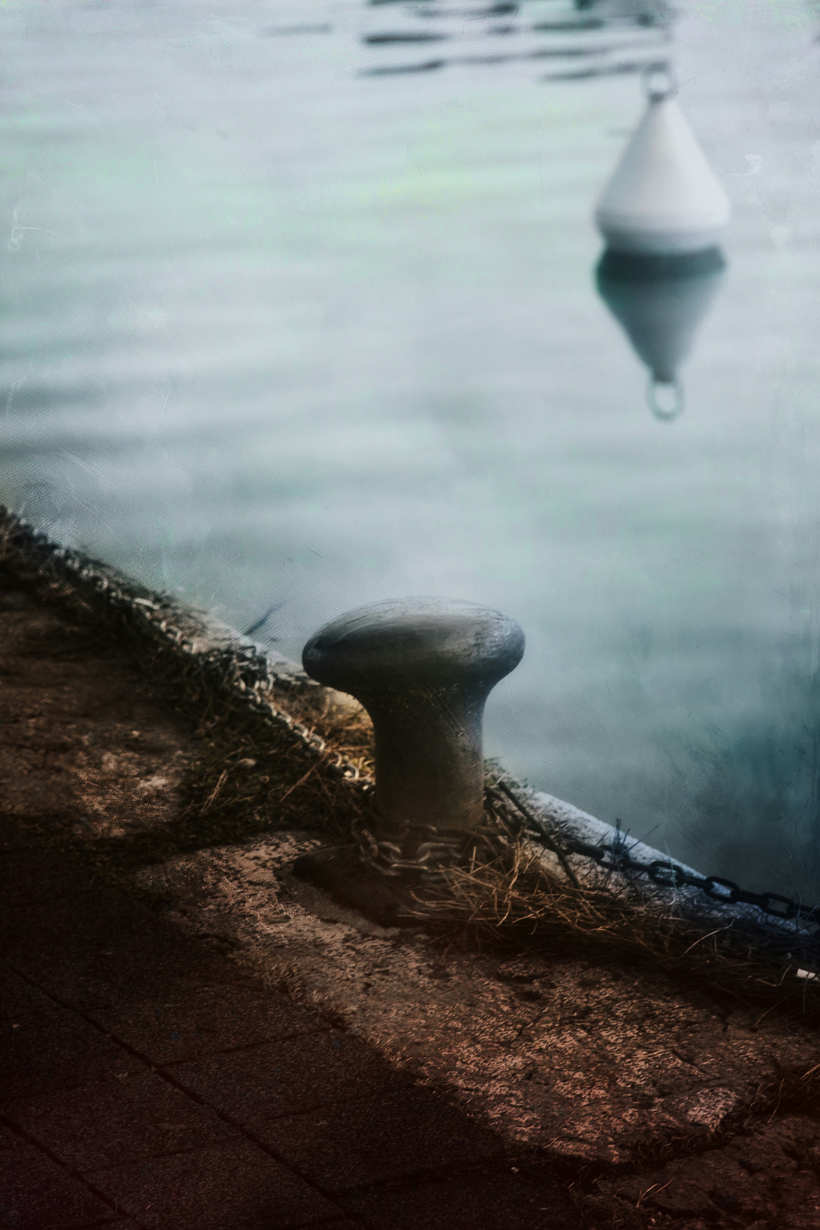 A bollard and chain on a dock with a buoy.