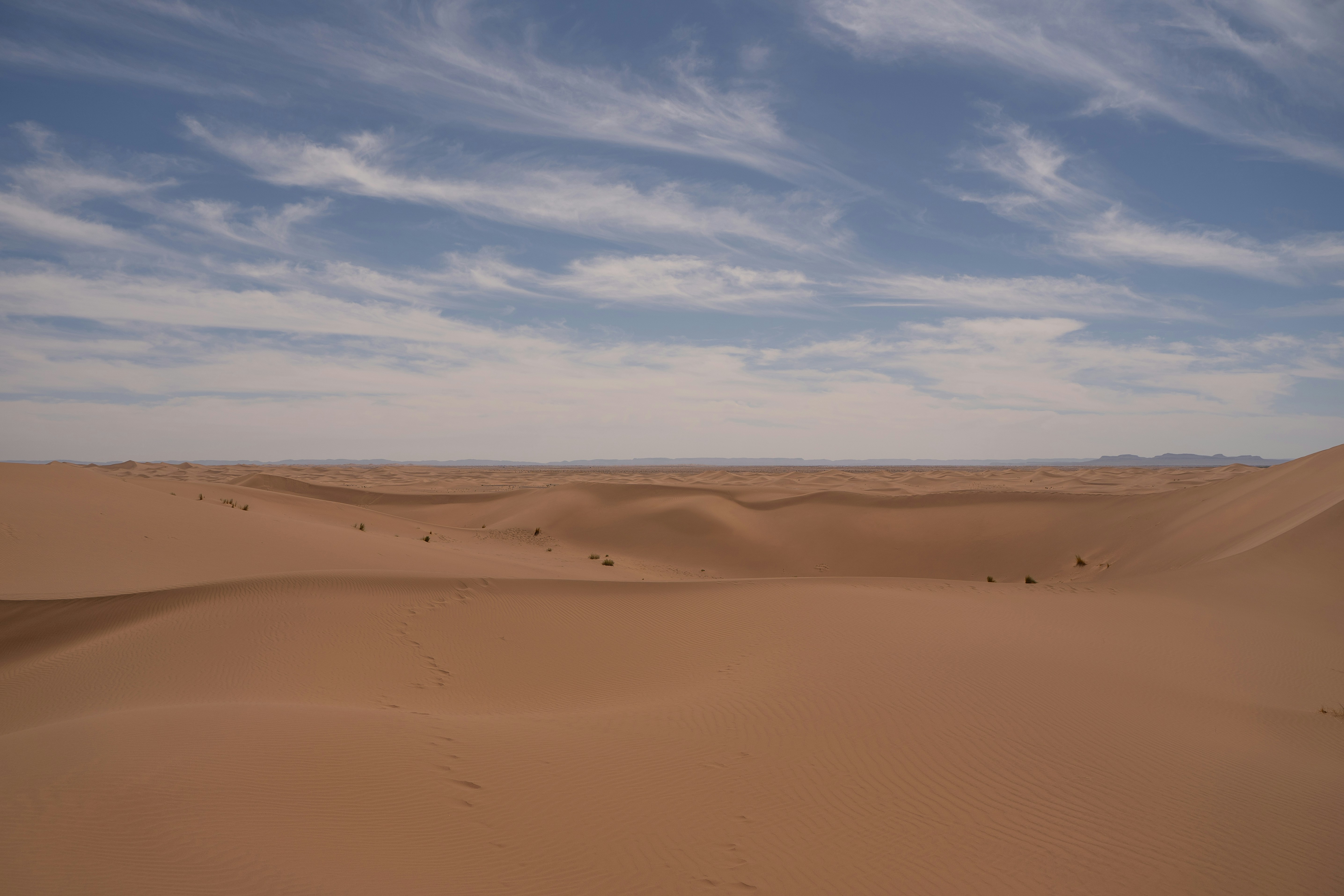 Vast desert dunes under a cloudy blue sky