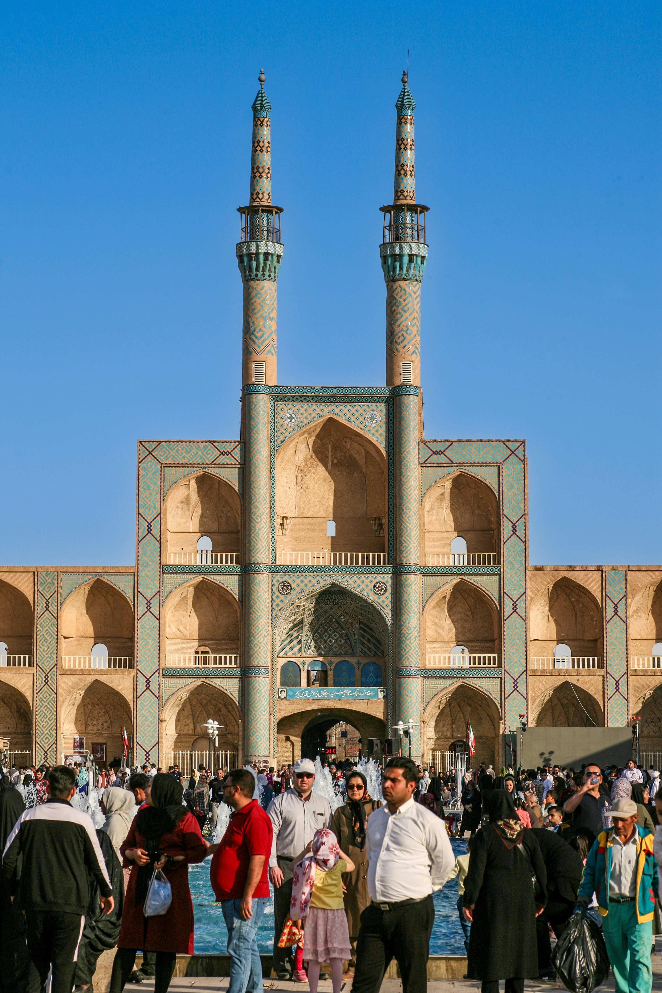 Crowd gathered in front of a mosque with twin minarets.