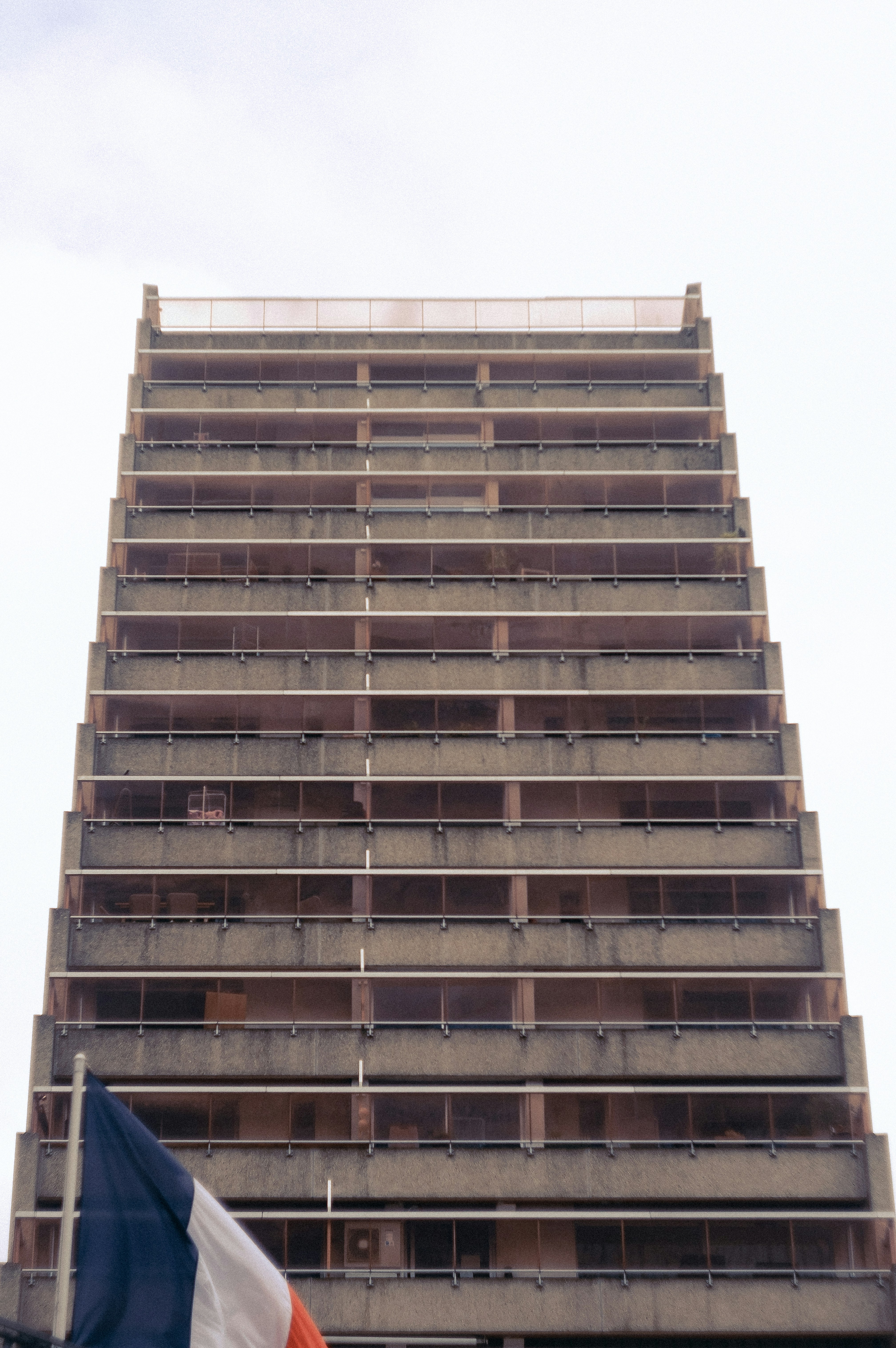 Tall concrete building with balconies and french flag.