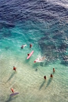 People surfing and swimming in clear turquoise ocean water.