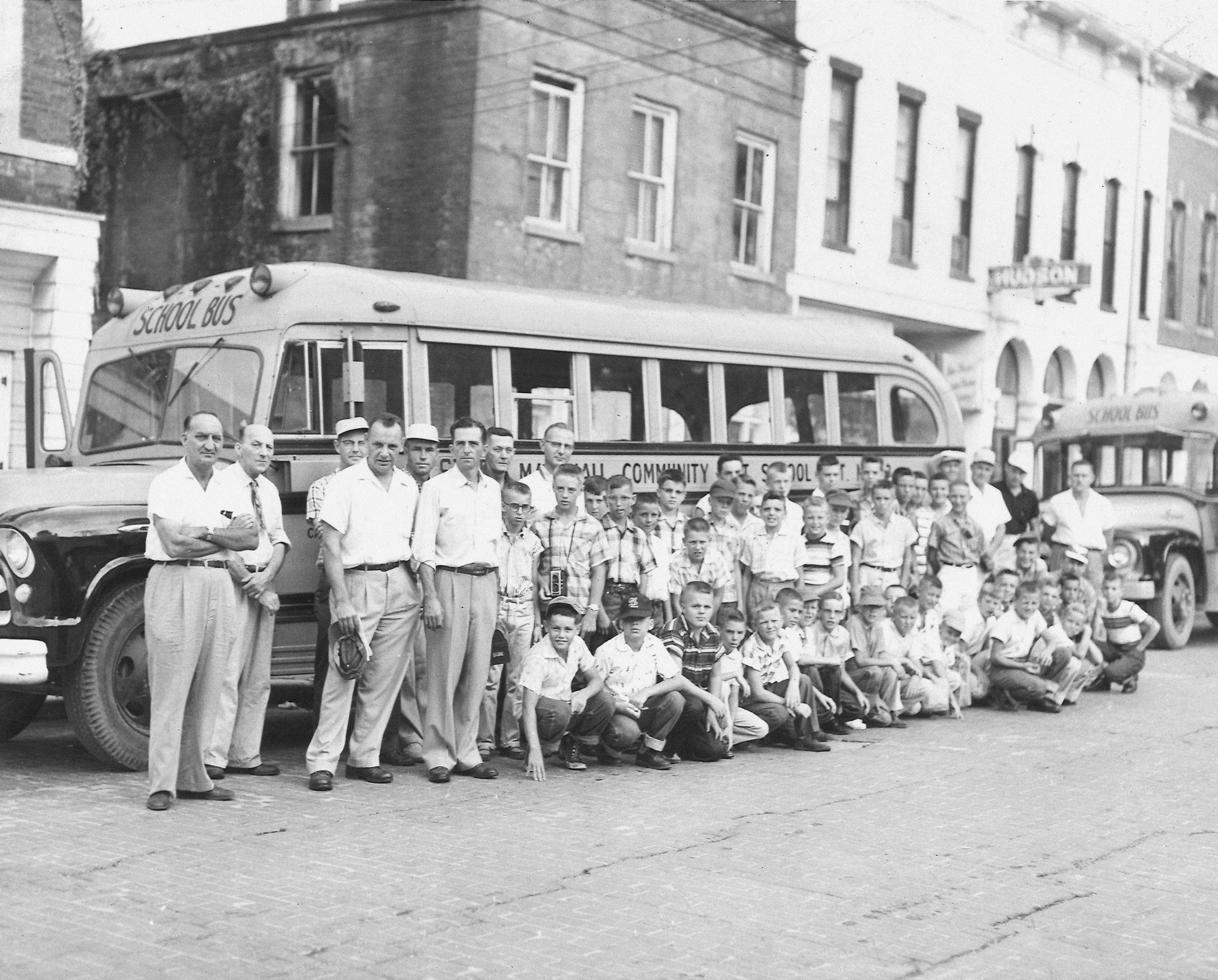 Group of boys and men pose by a school bus.