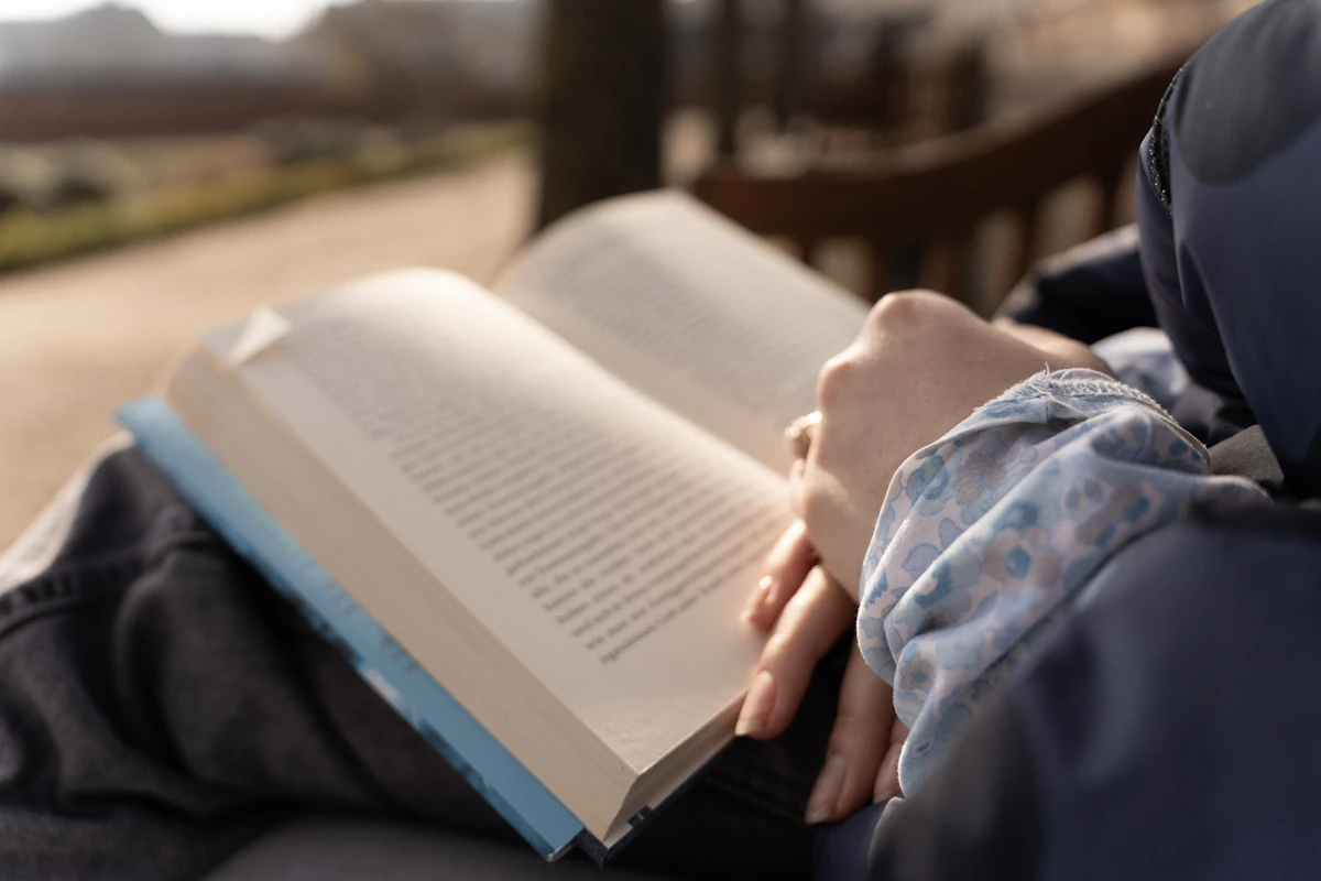 Eine Person liest draußen auf einer Bank ein geöffnetes Buch