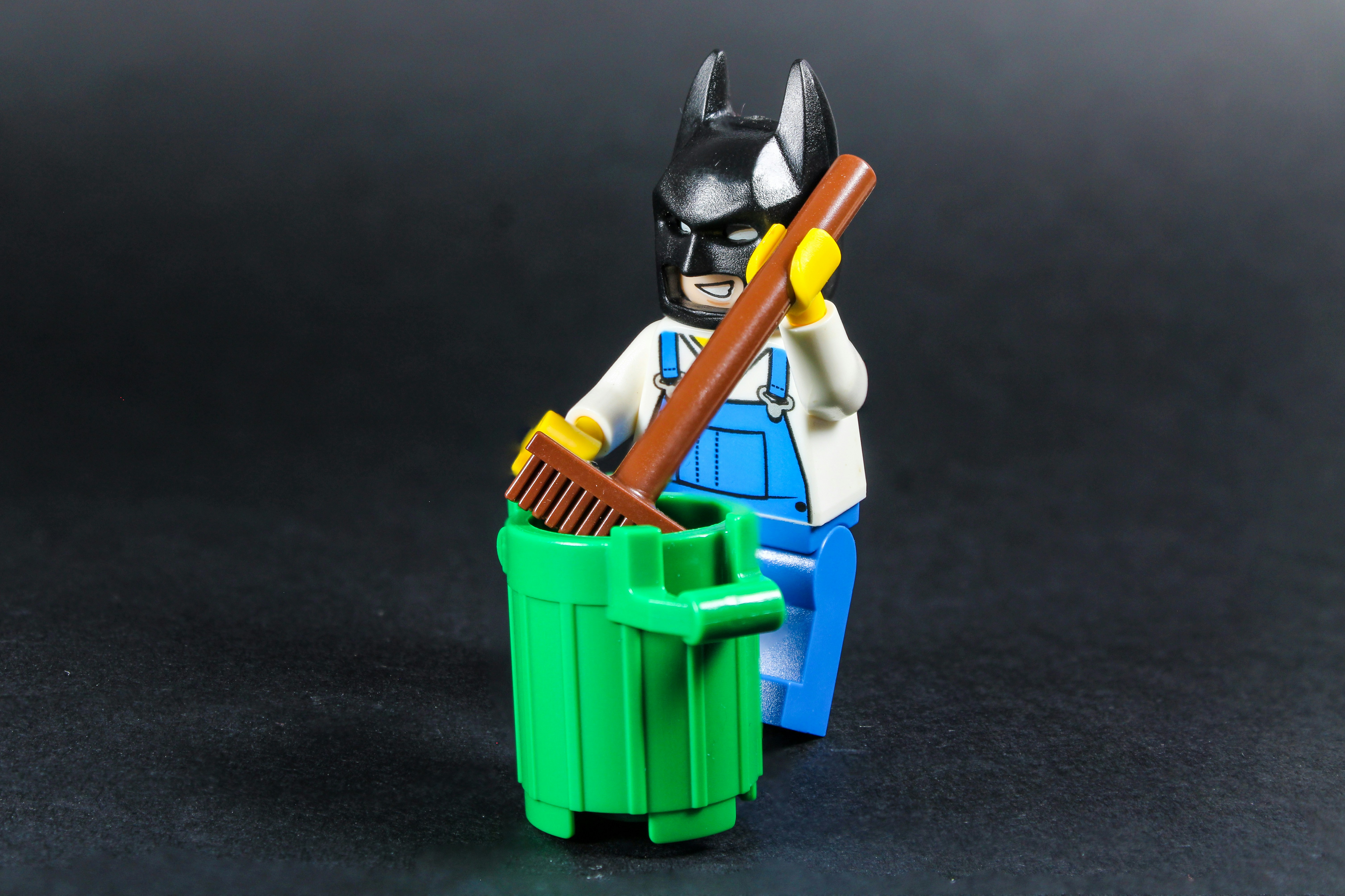 Lego batman figure cleans green trash can with broom