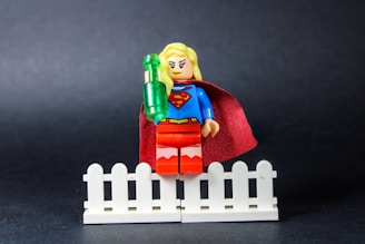 Supergirl lego figure holding a green bottle on fence.