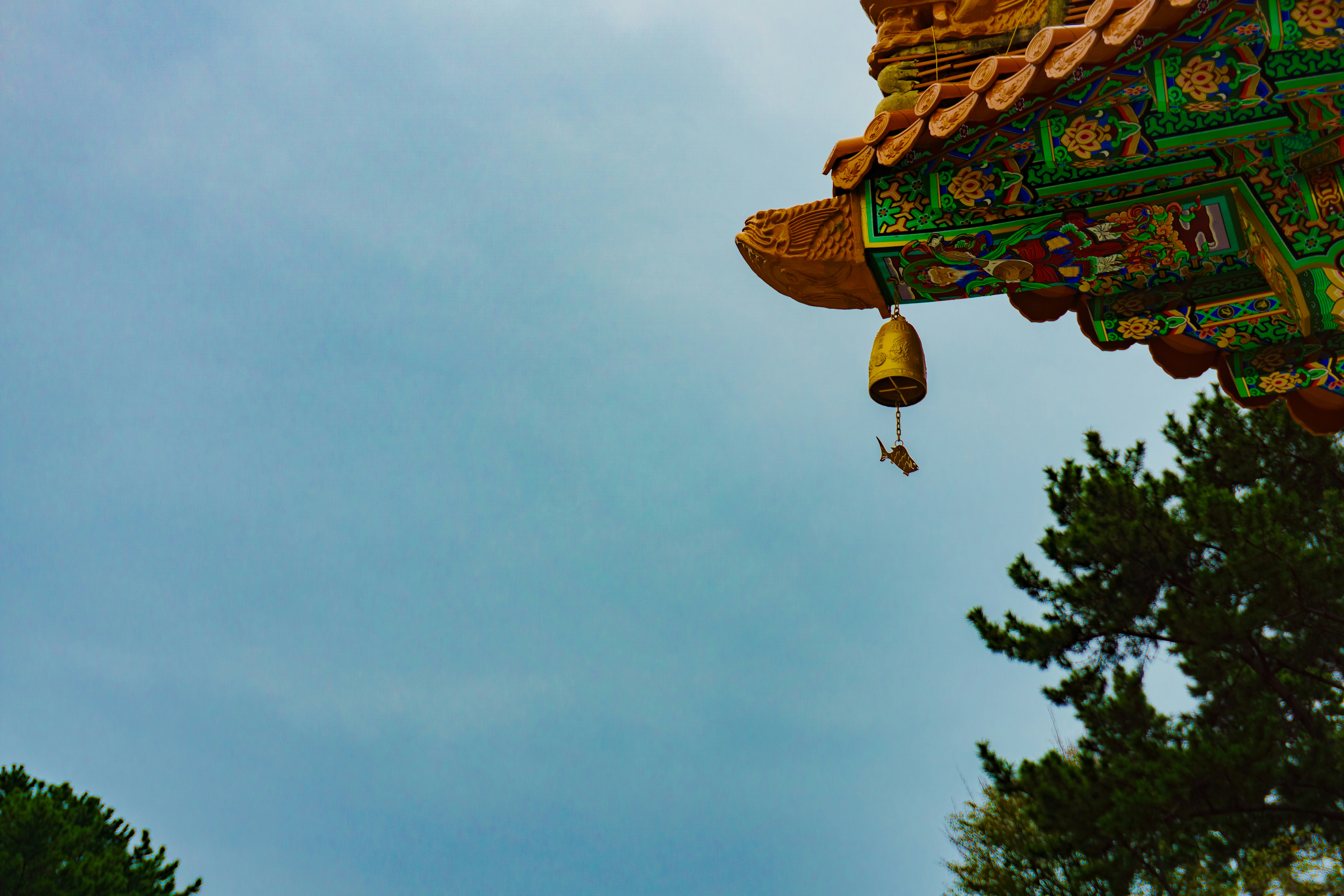 Ornate temple eaves with hanging bell and sky.