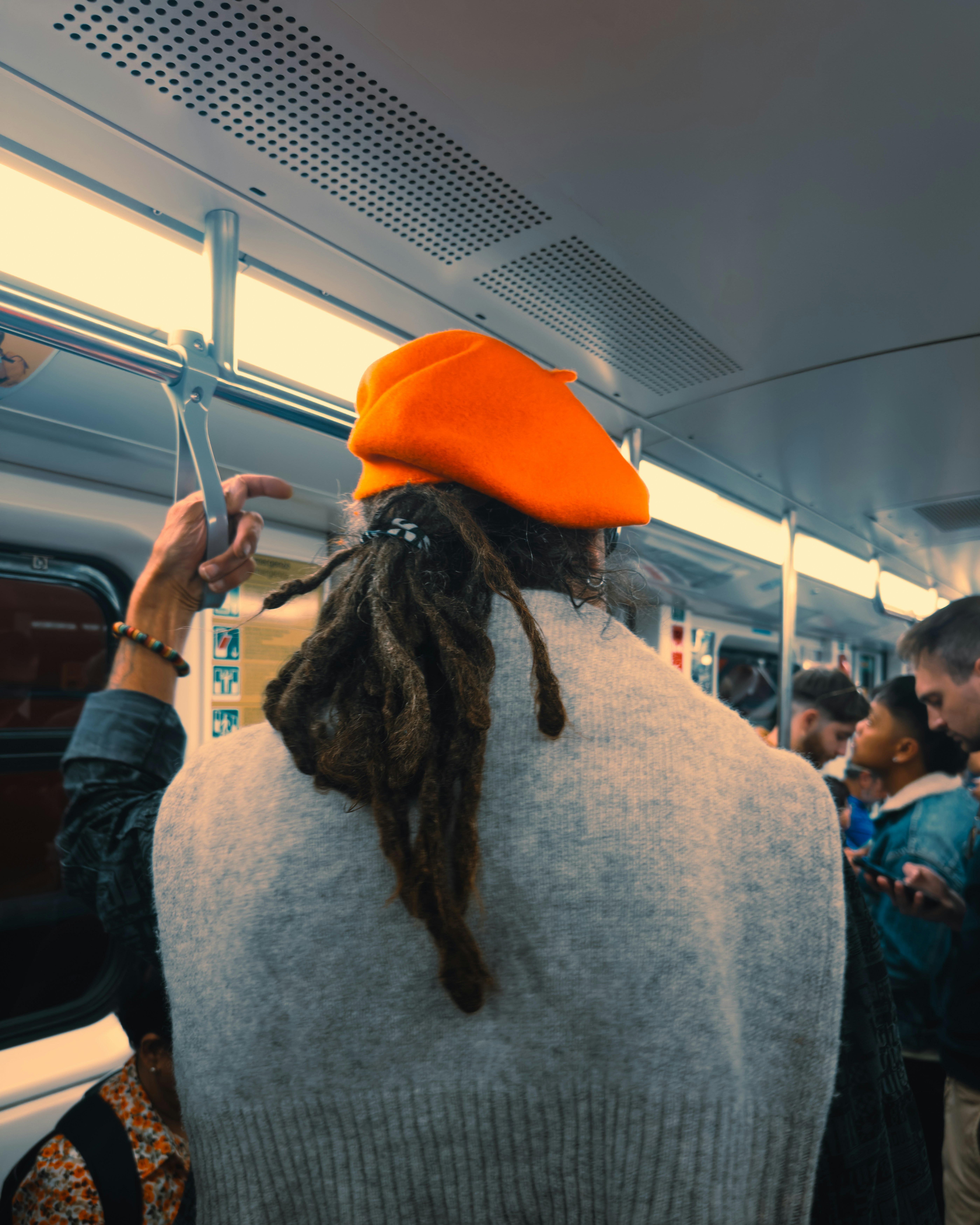 Person with dreadlocks wearing an orange beret on a train.