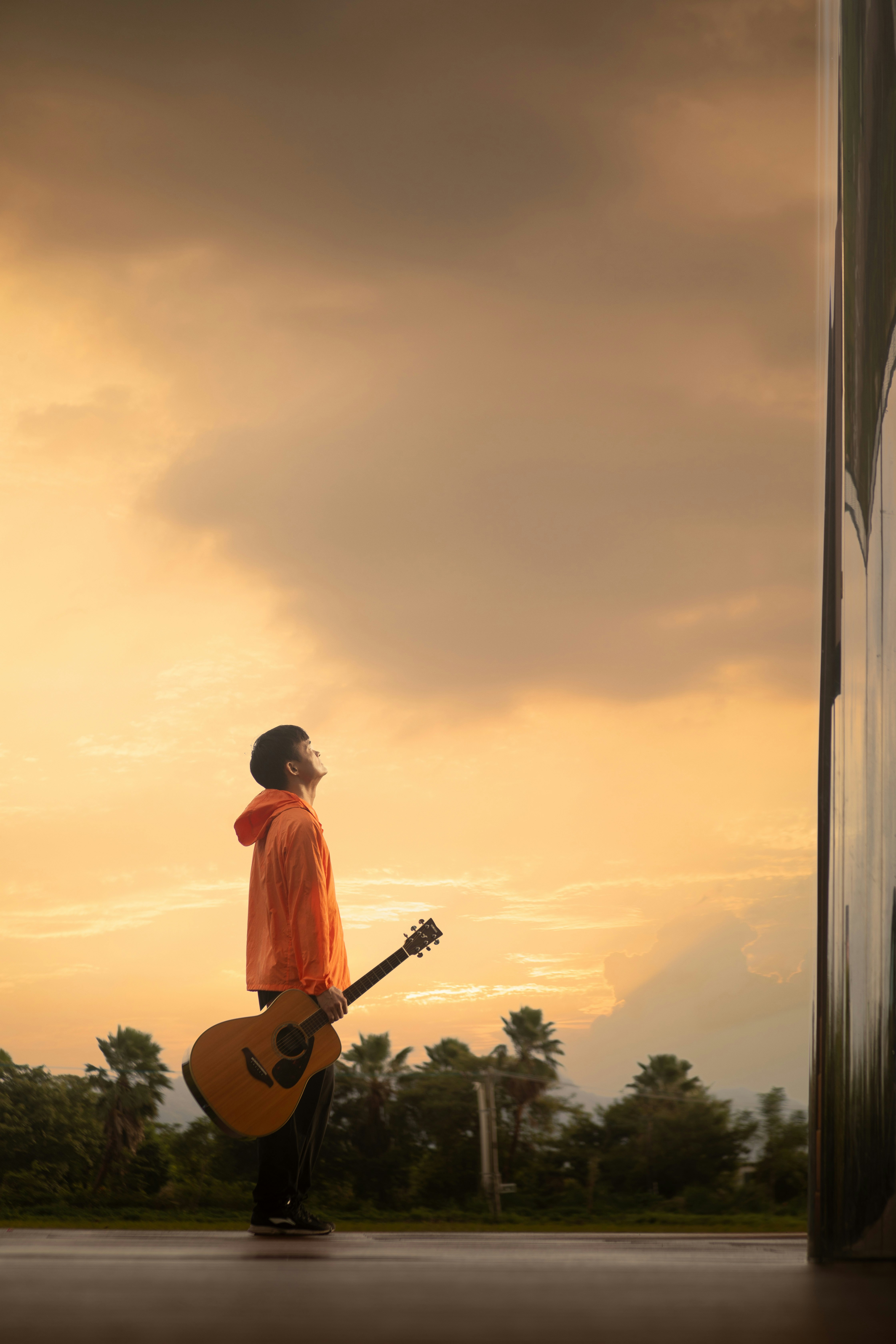 Man in orange hoodie holding guitar at sunset