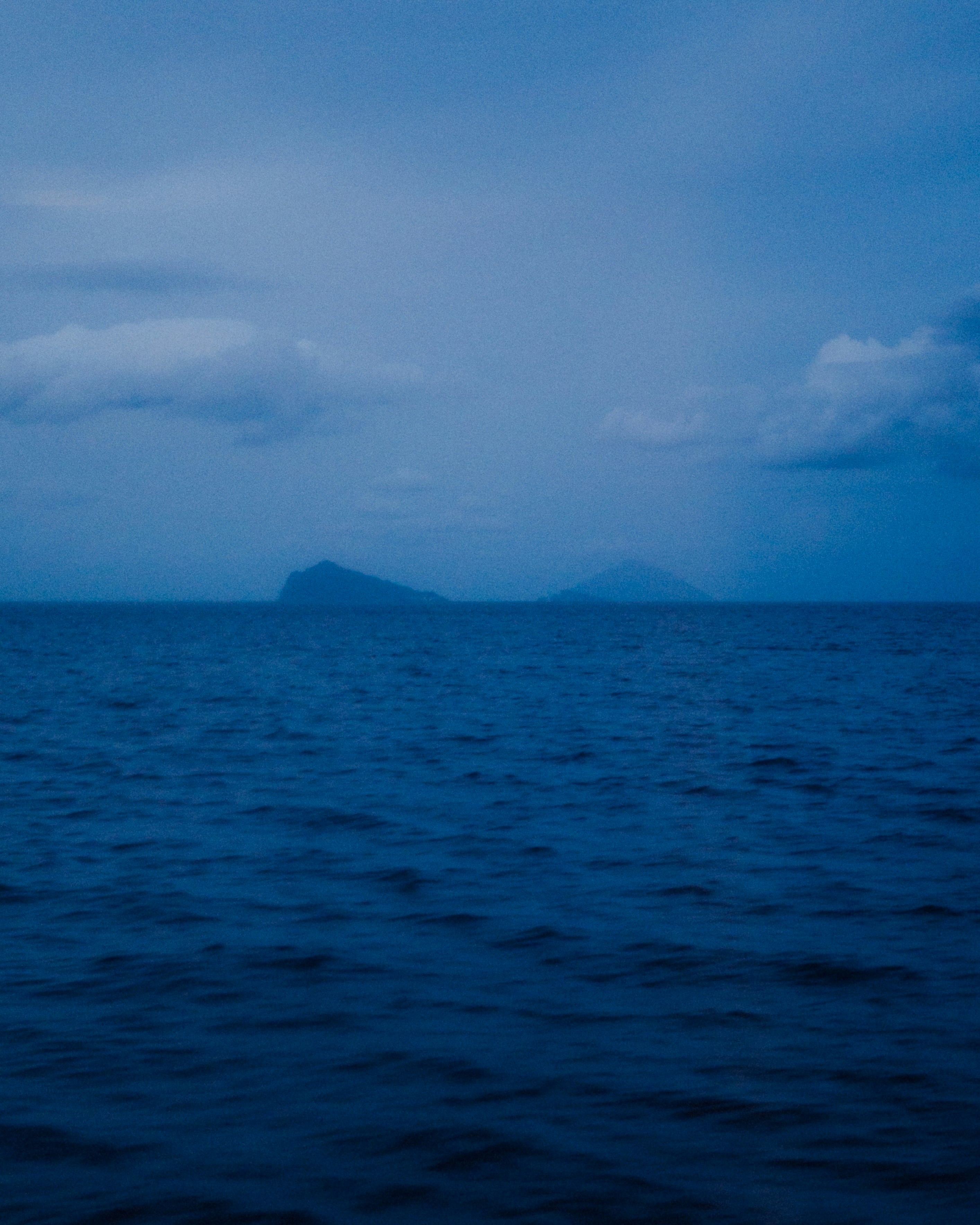 Distant islands on a dark blue ocean under cloudy sky.