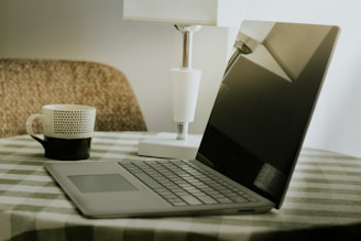 Laptop and coffee cup on a checkered tablecloth.