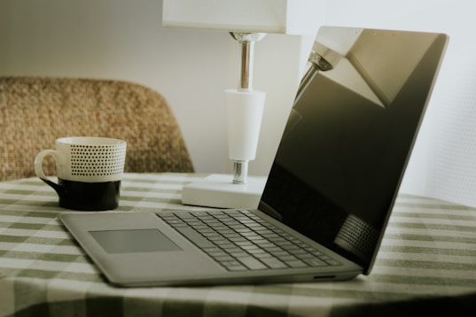 Laptop and coffee cup on a checkered tablecloth.
