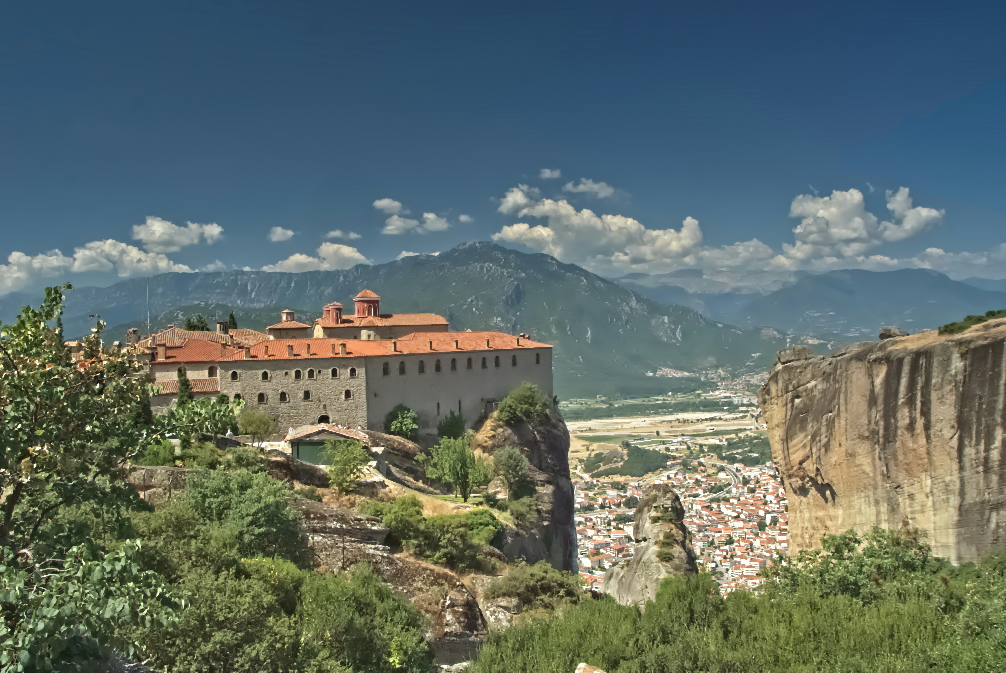 Monastery perched on a rocky cliff overlooking a town.