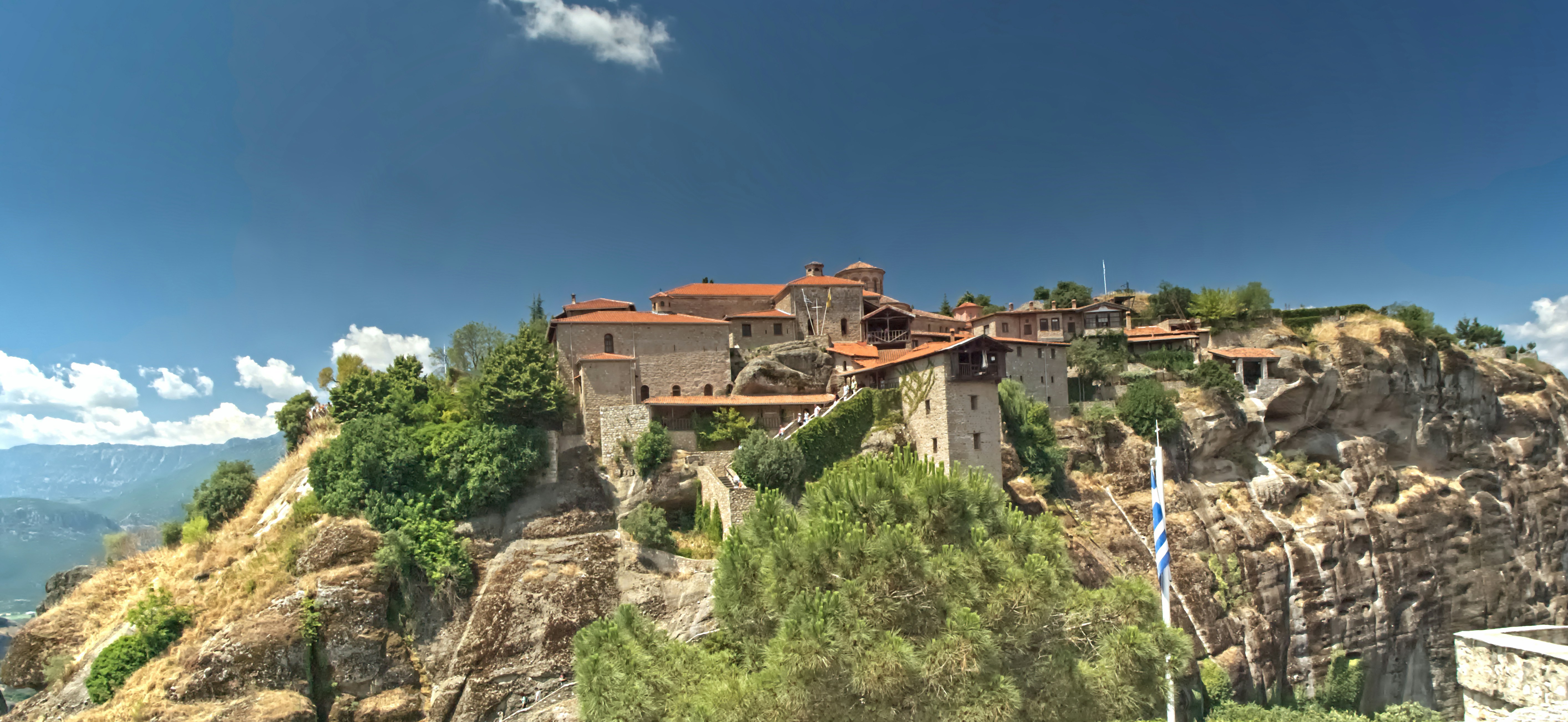 Monastery complex built on a rocky cliff under blue sky.