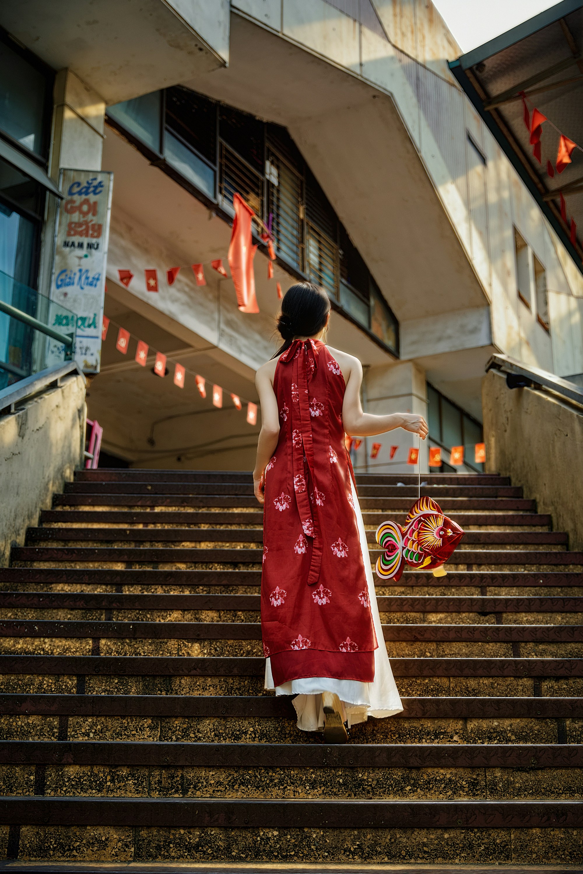 Woman in red dress climbs stairs with lanterns.