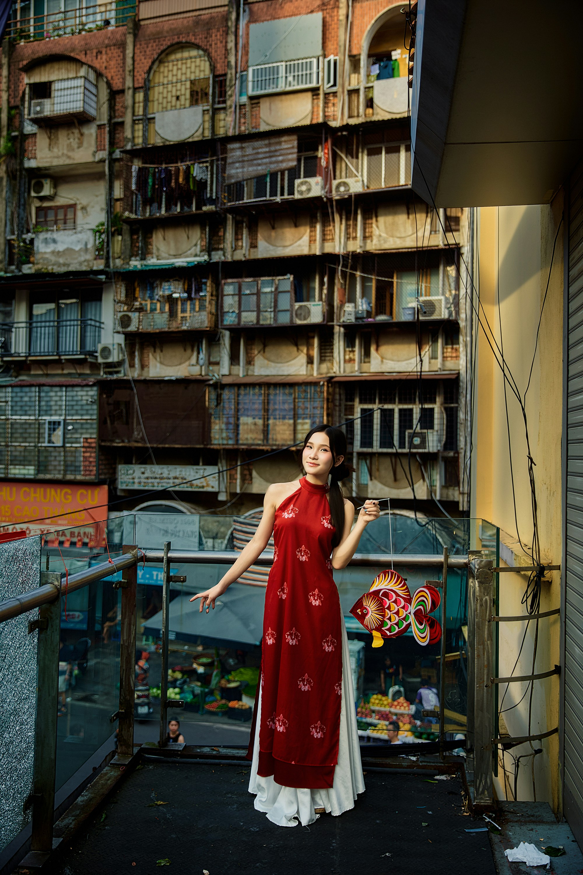 Woman in traditional dress stands on balcony with cityscape.