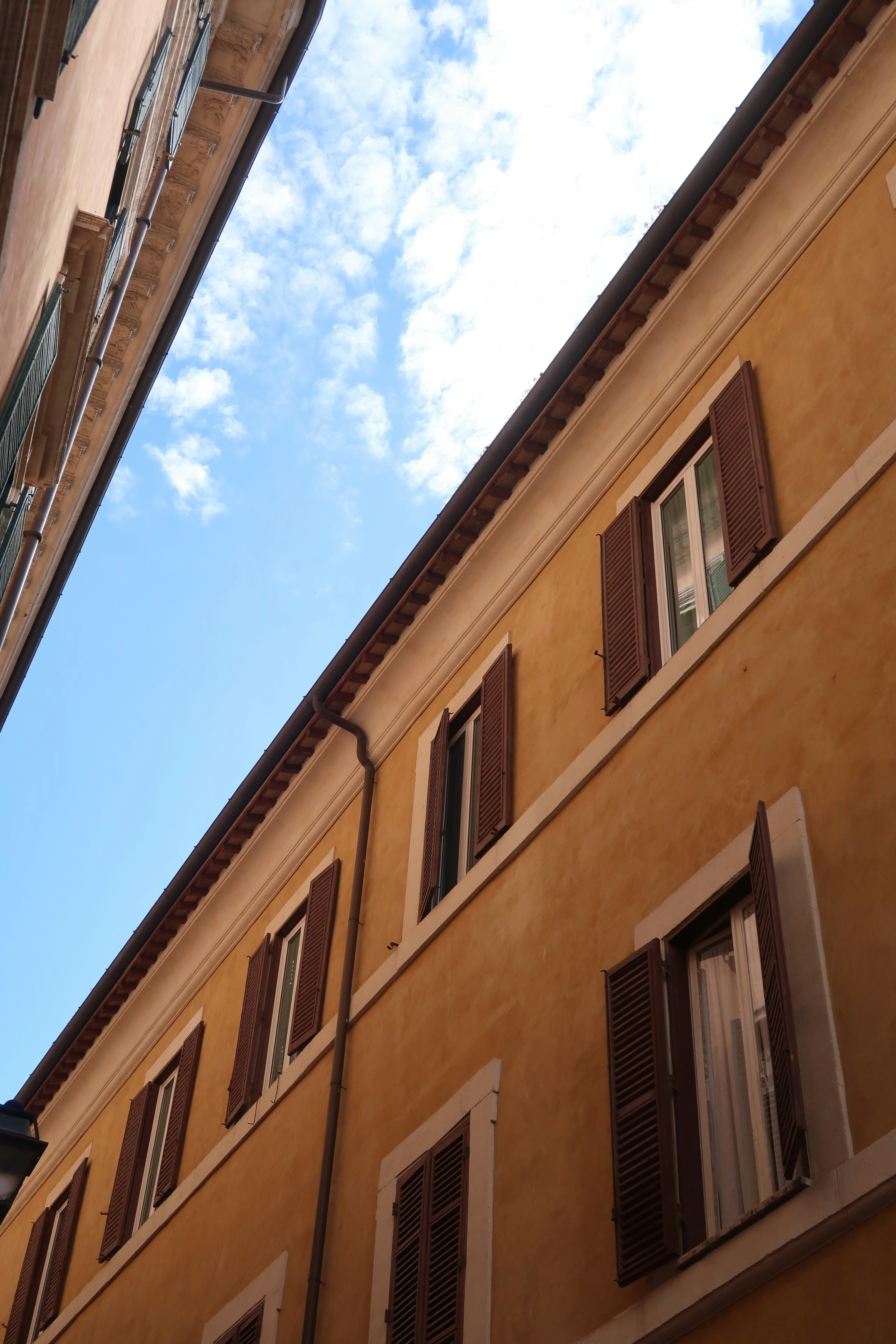 Yellow building facade with open shutters against blue sky.