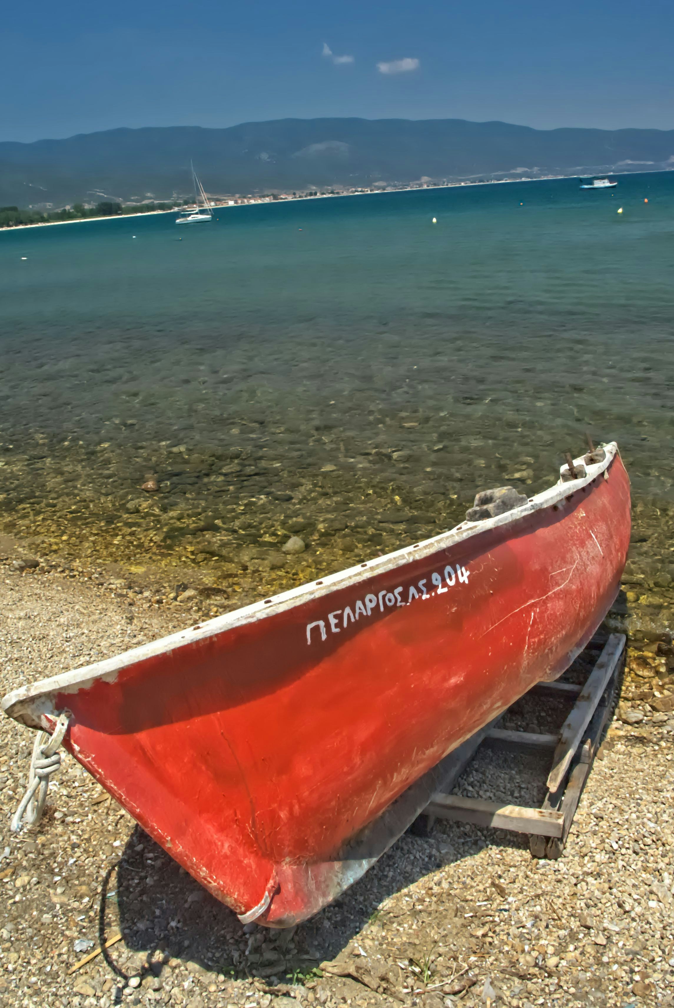 Red rowboat resting on a pebble beach by the sea.