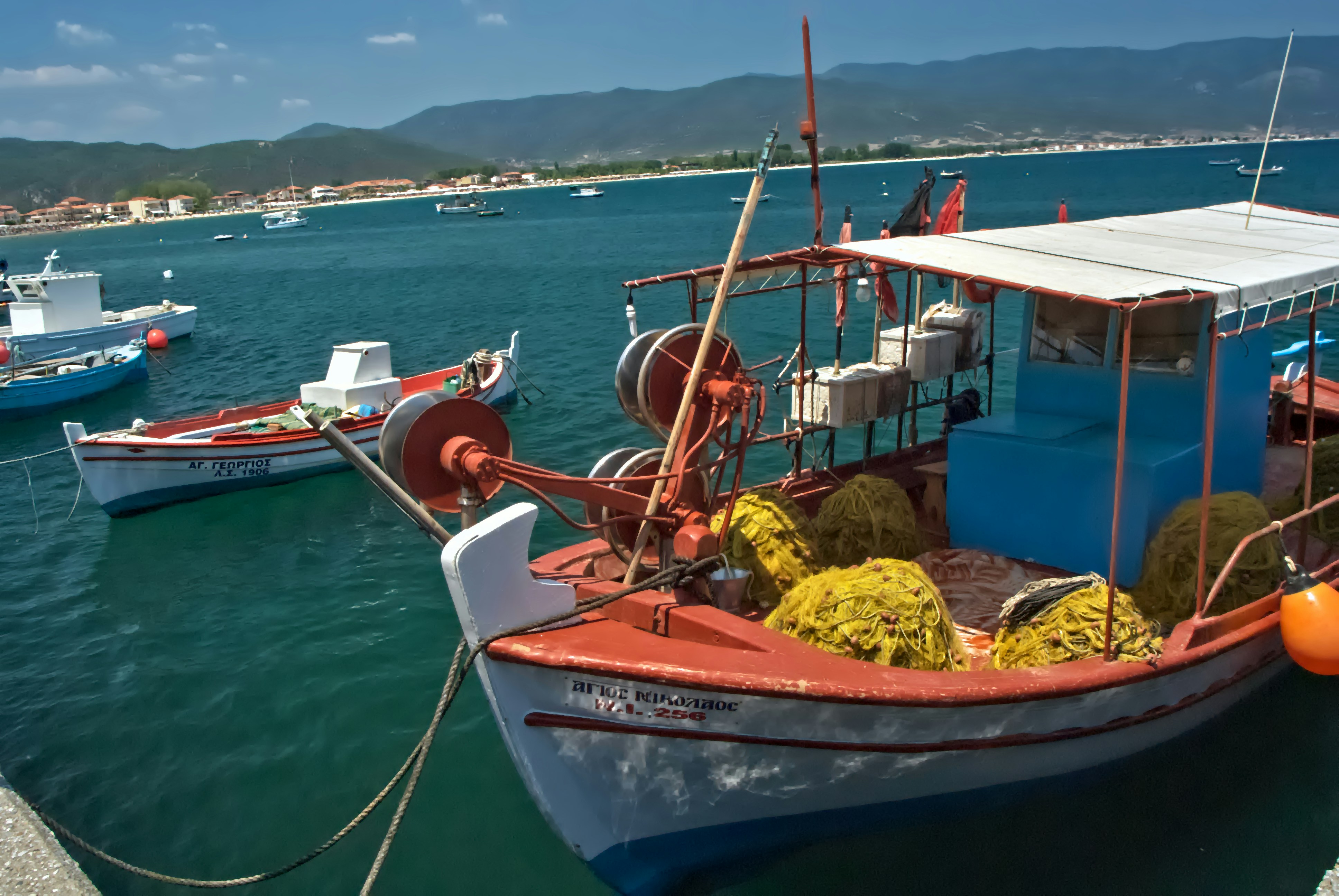 Fishing boats docked in a sunny harbor with blue water.
