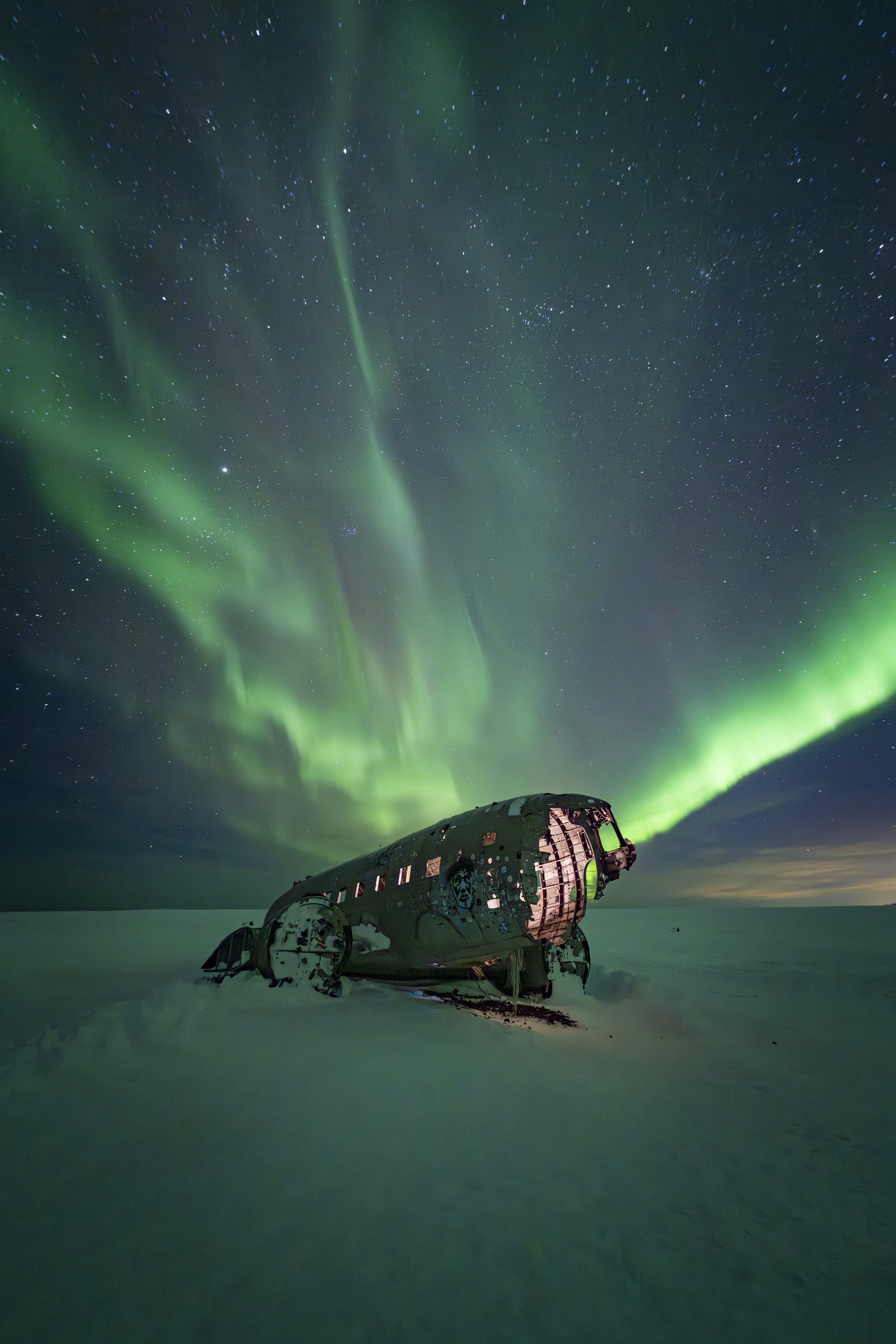 Aurora borealis over a crashed airplane in snow.
