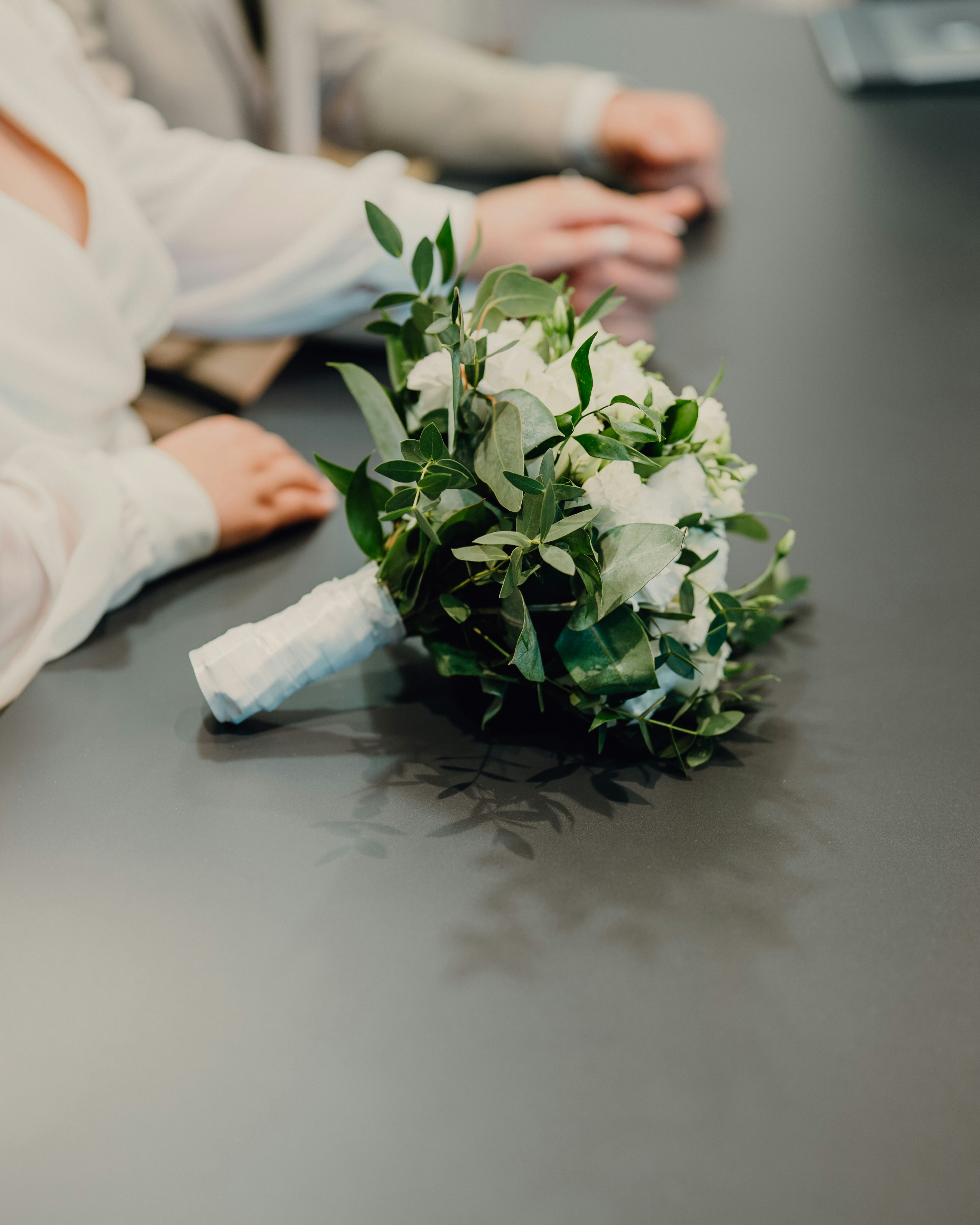 Bridal bouquet with white flowers and eucalyptus rests on a table.
