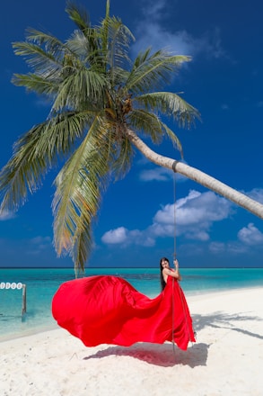 Woman in red dress on a swing under palm tree