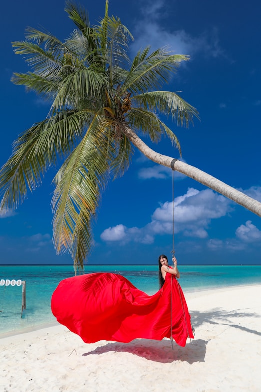 Woman in red dress on a swing under palm tree