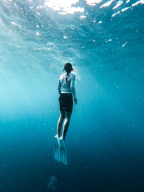Woman with fins swims underwater in blue ocean
