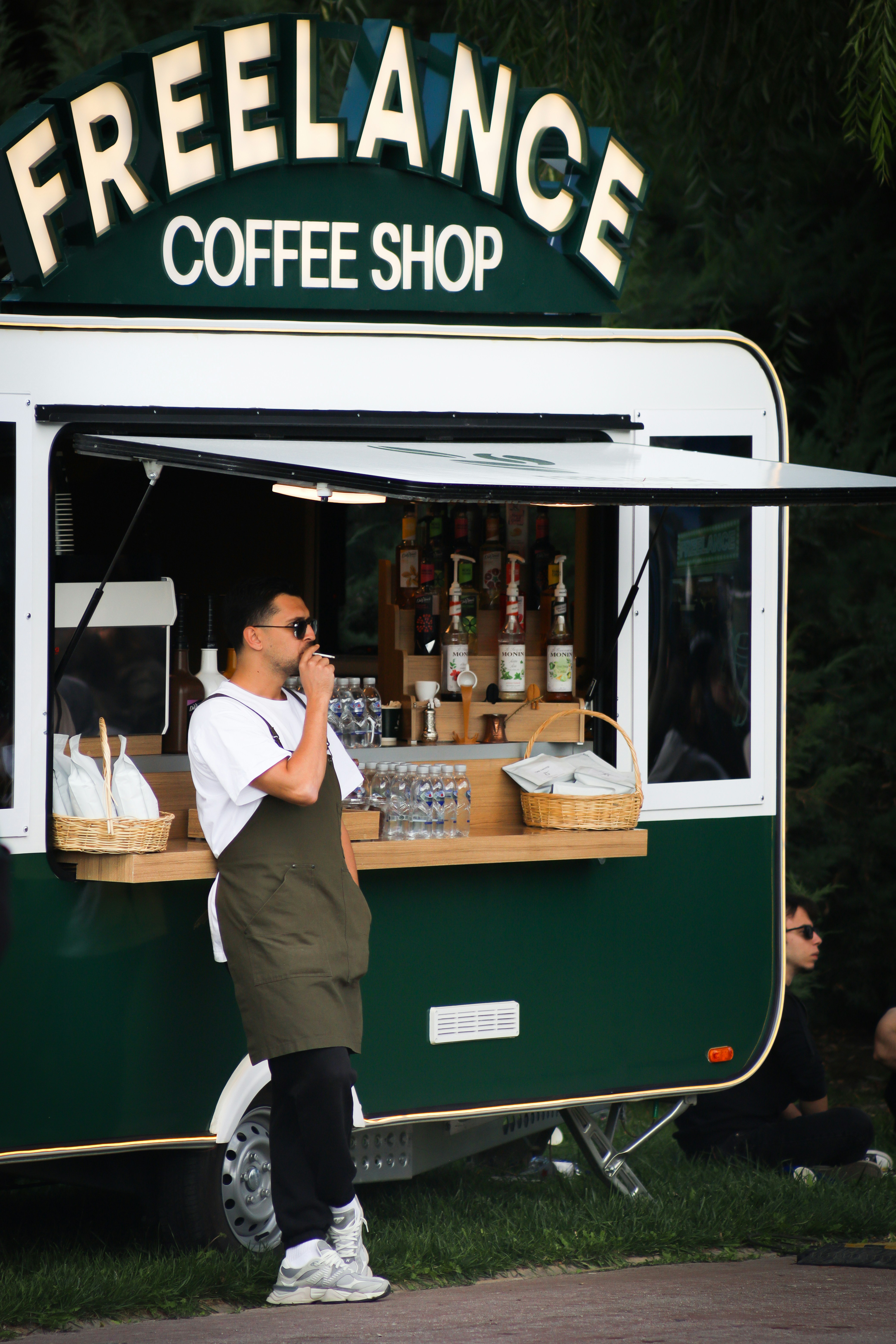 Barista, der vor einem grünen Coffeeshop-Wohnwagen raucht.