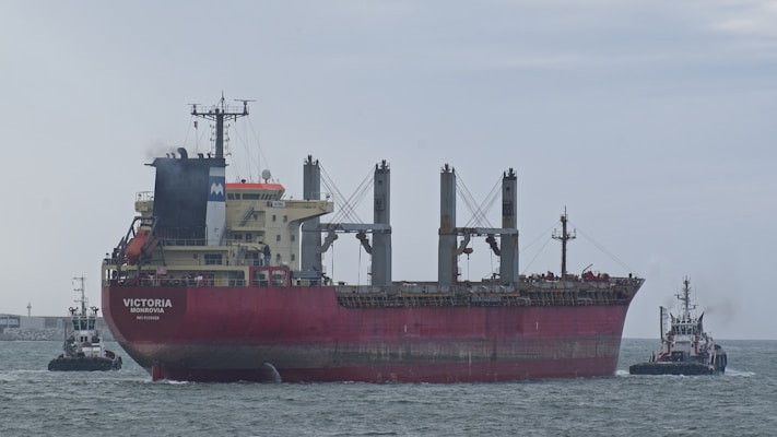 Large red cargo ship guided by two tugboats at sea