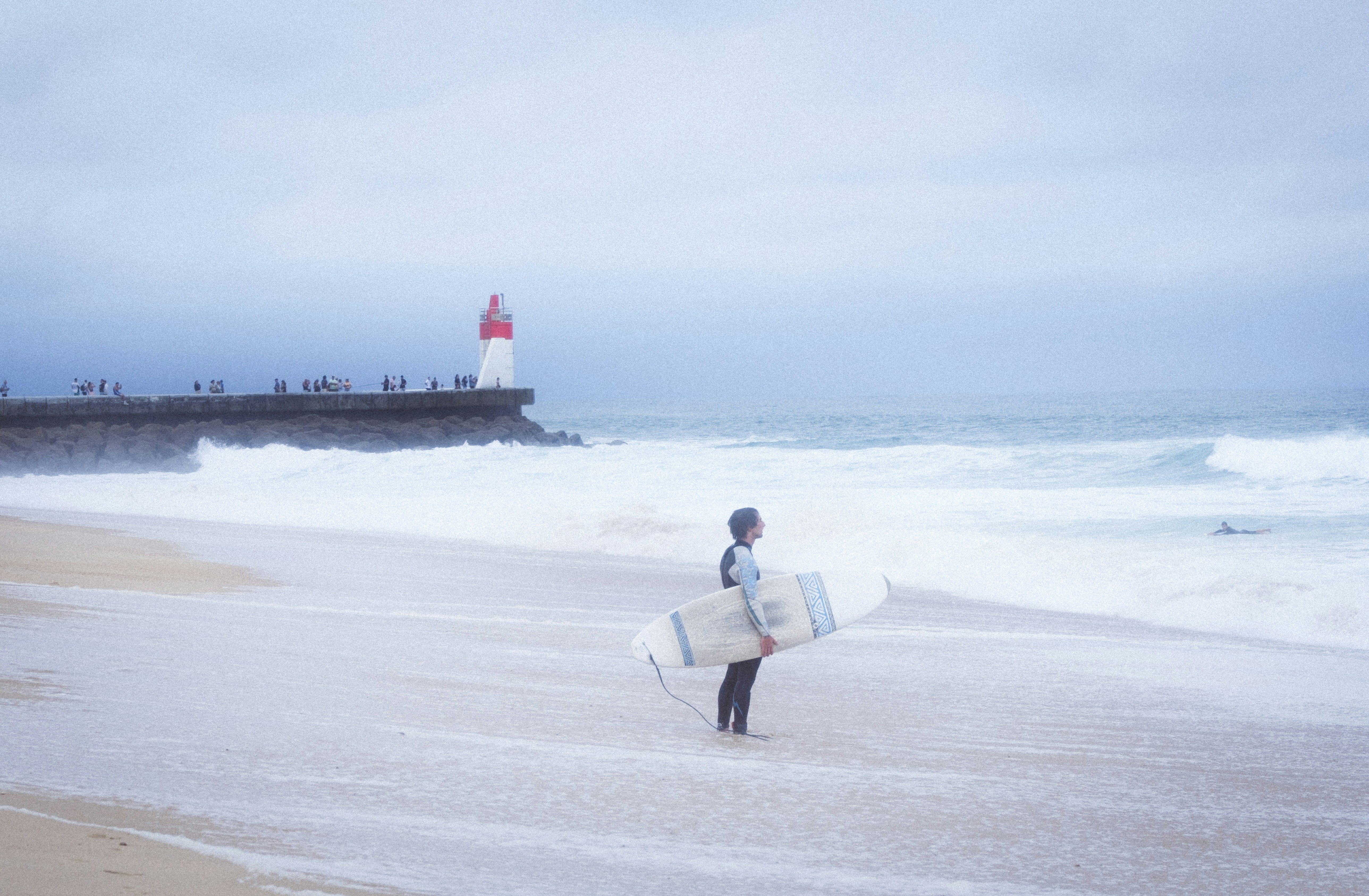 Surfista con tabla en la playa cerca del faro.