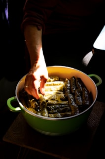 Hands arranging stuffed grape leaves in a pot.