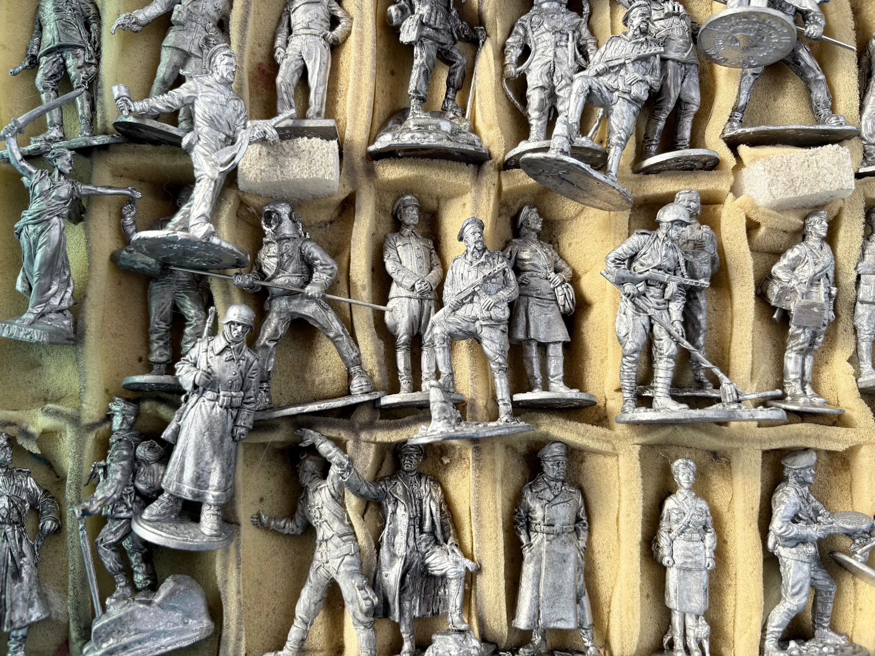 Rows of unpainted gray metal soldier figures standing in a foam tray
