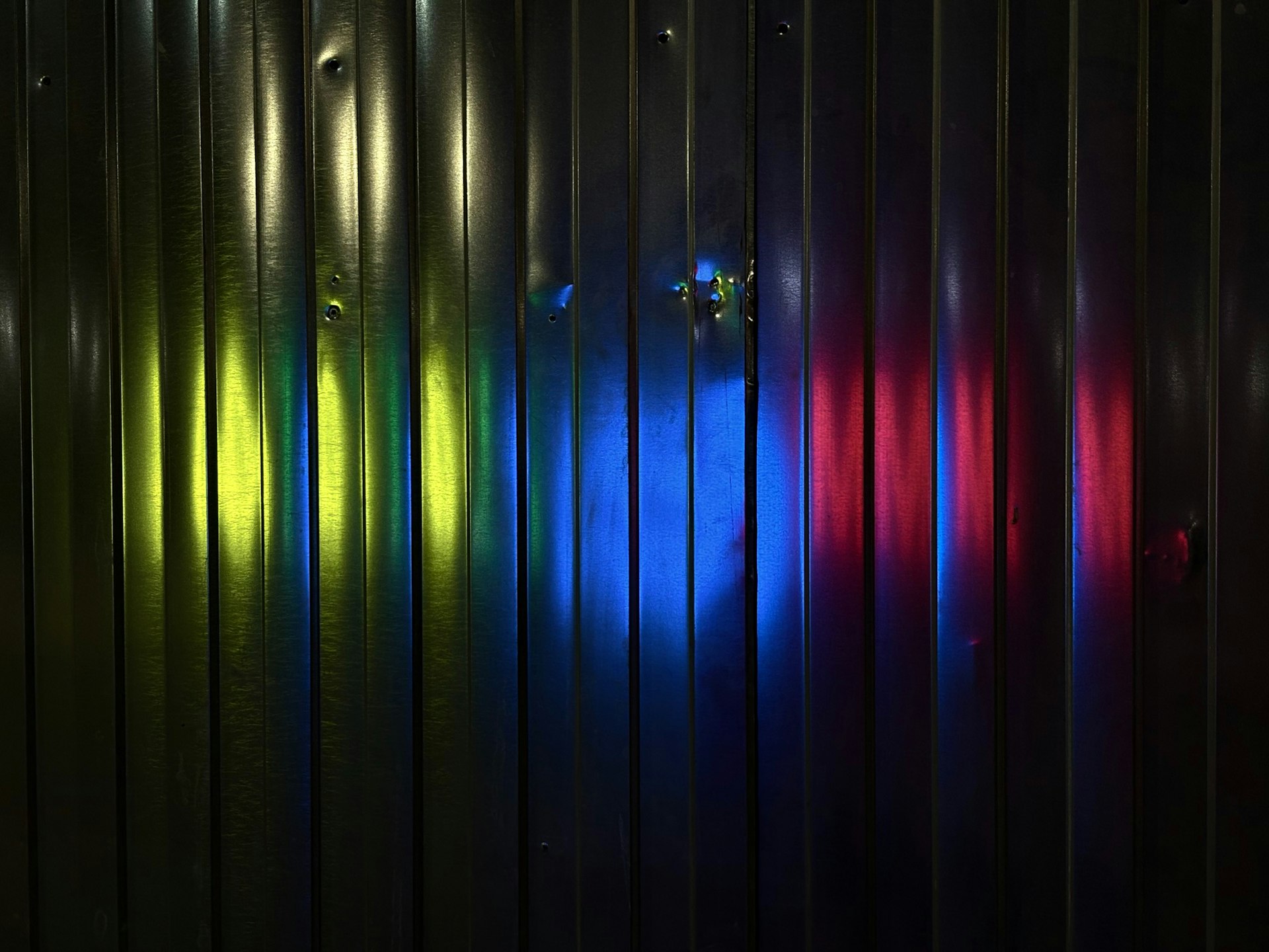 Corrugated metal wall with colorful light reflections.