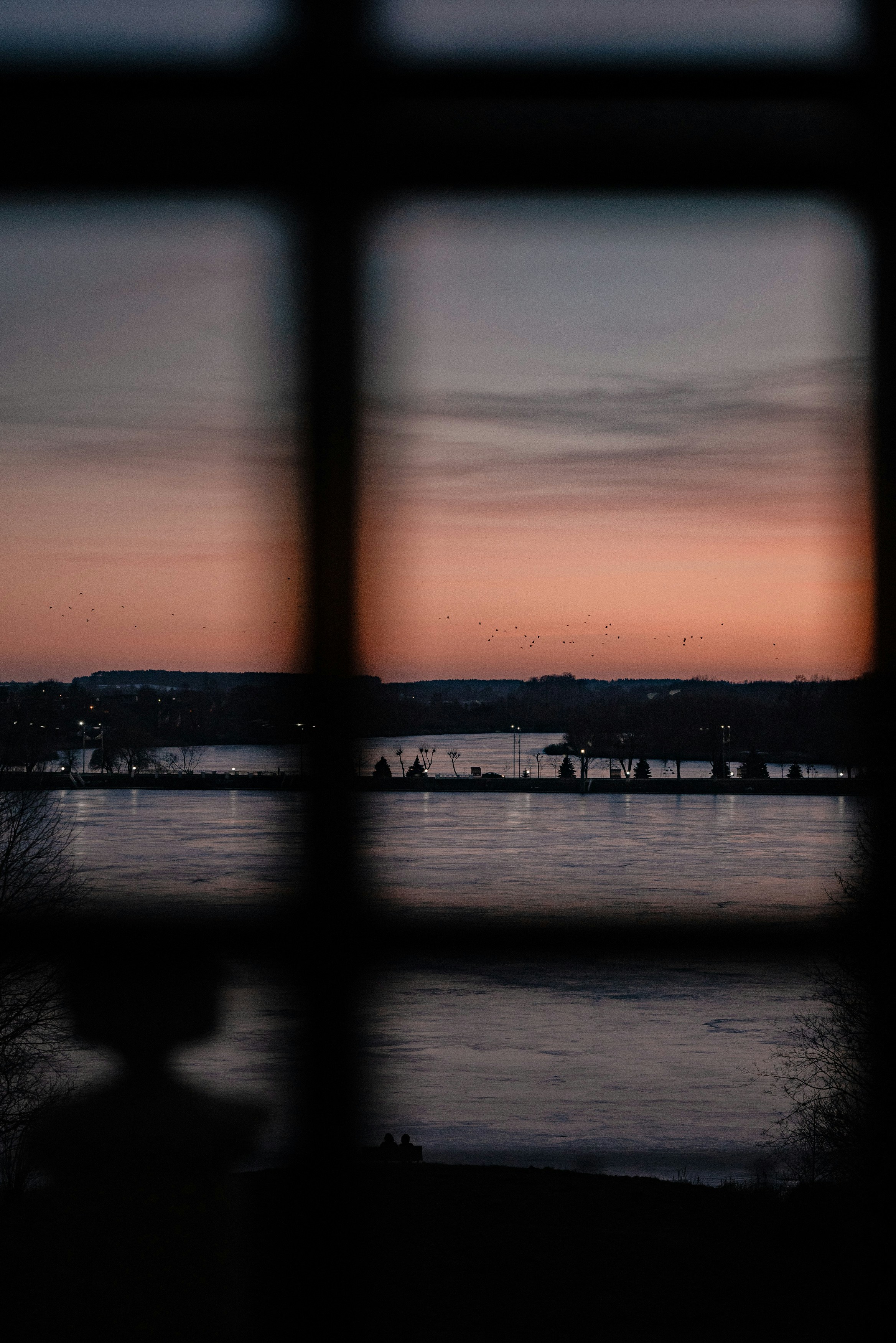 Sunset over a calm body of water viewed through window.