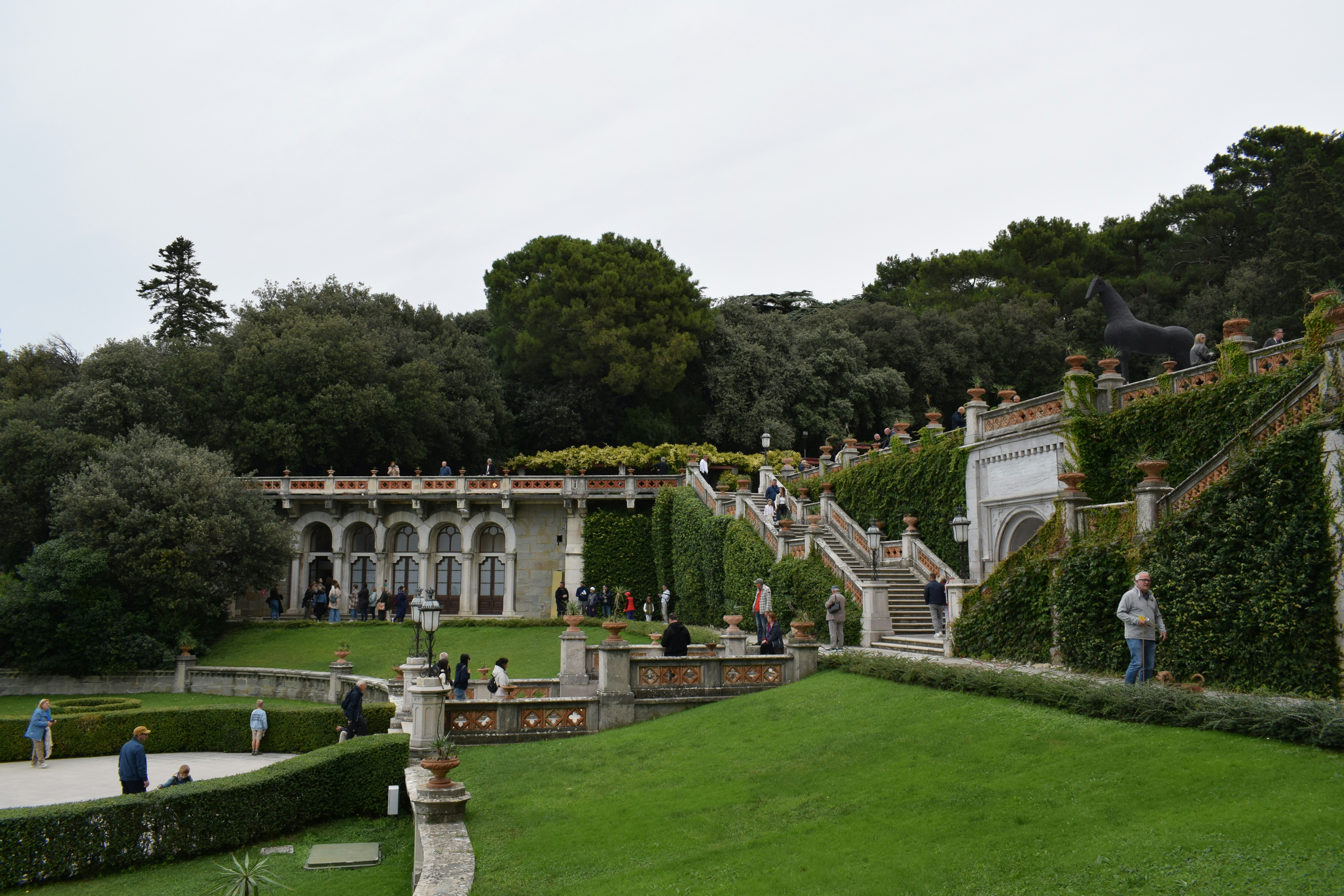 People explore a grand italian garden with stairs and greenery.
