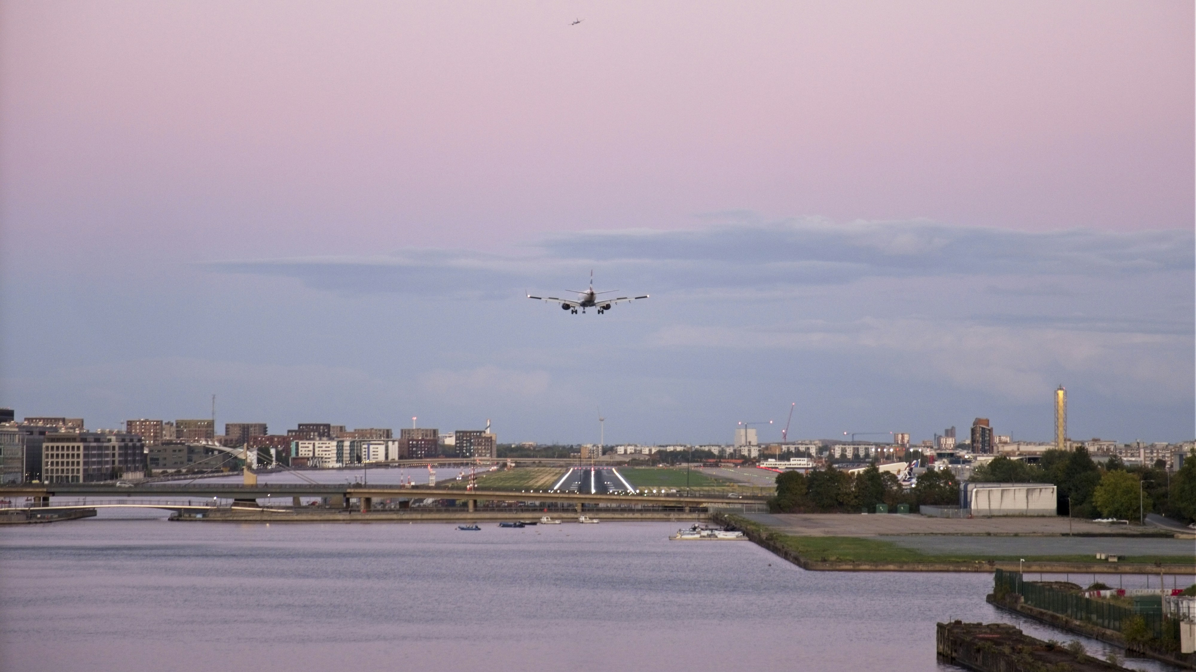Commercial airplane approaching a runway over a coastal cityscape at dusk