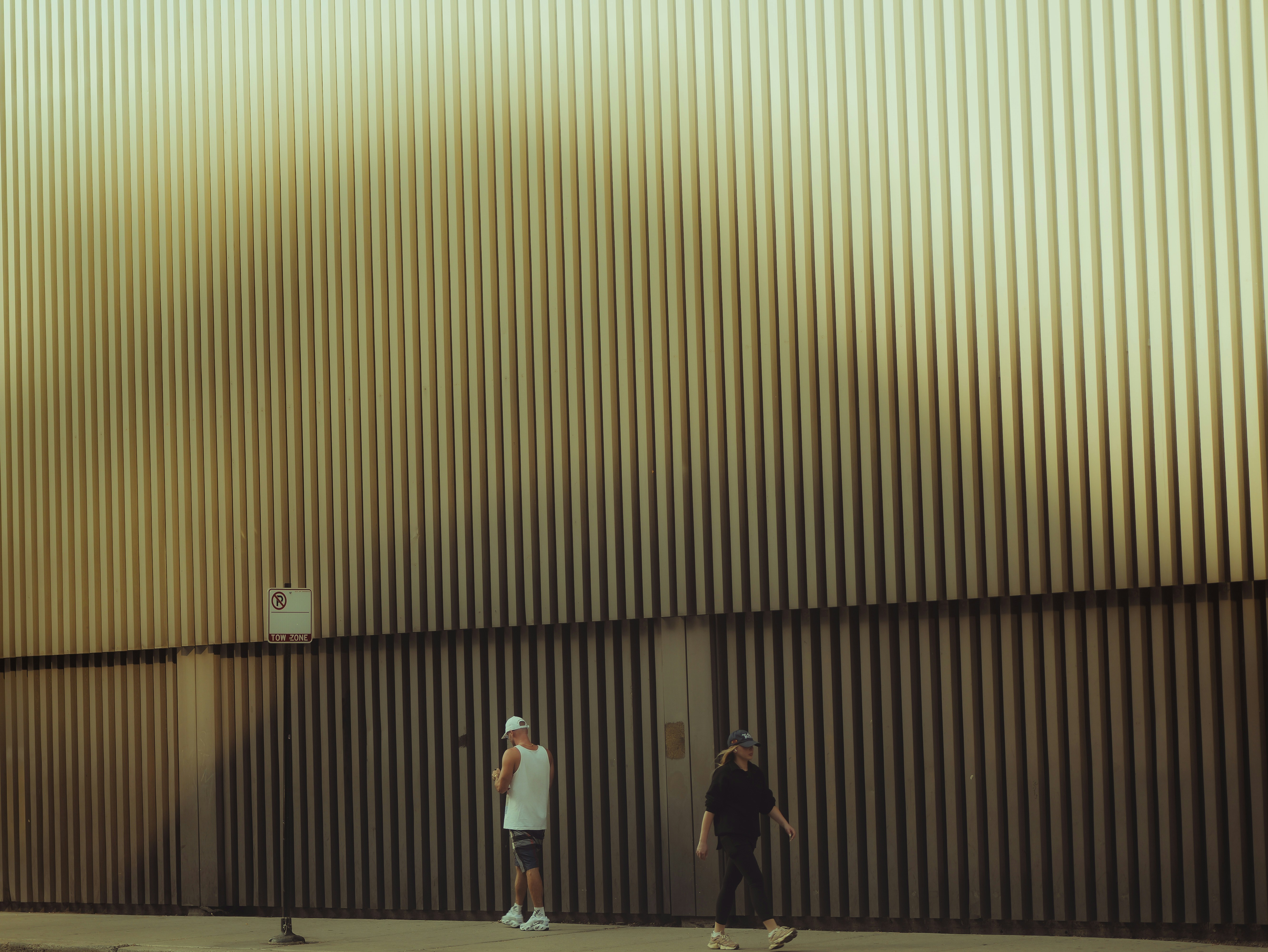 Two people stand against a corrugated metal wall.