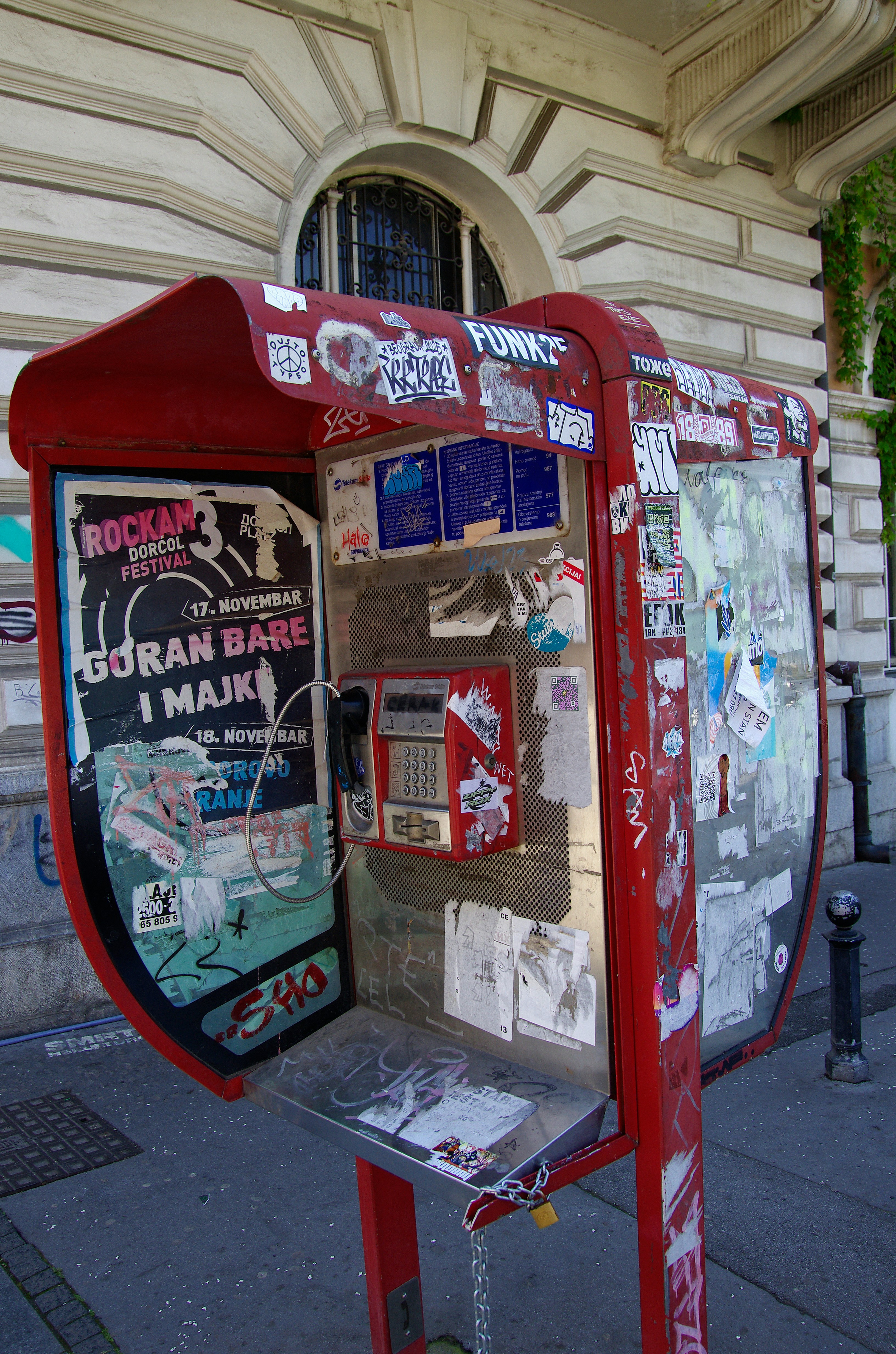 Red telephone booth covered in stickers and posters.