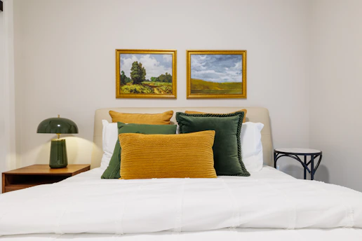 Bedroom with landscape paintings and green lamp.