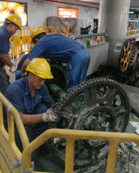 Workers in hard hats repair large industrial machinery gears.