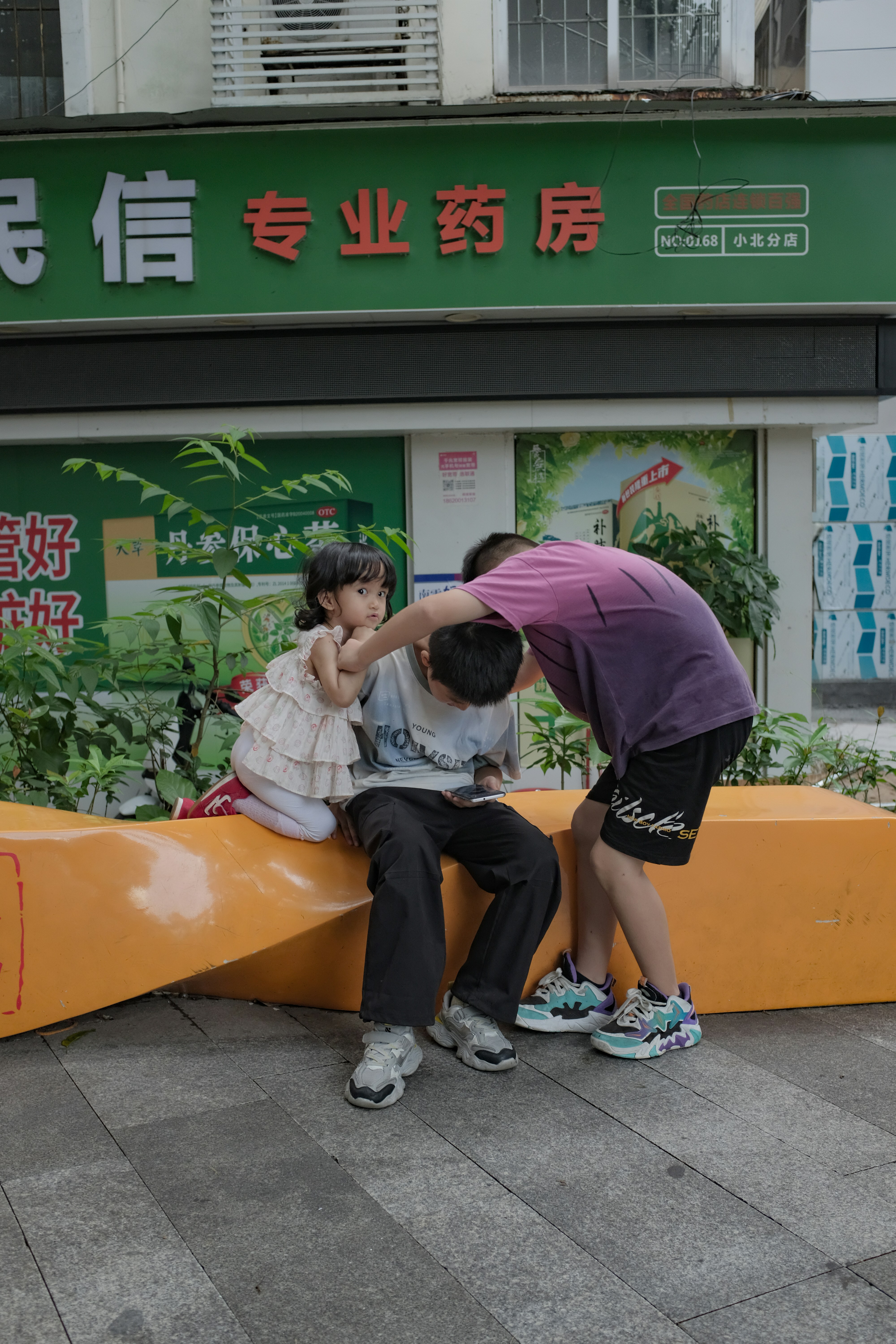 Three children interacting on a street bench.
