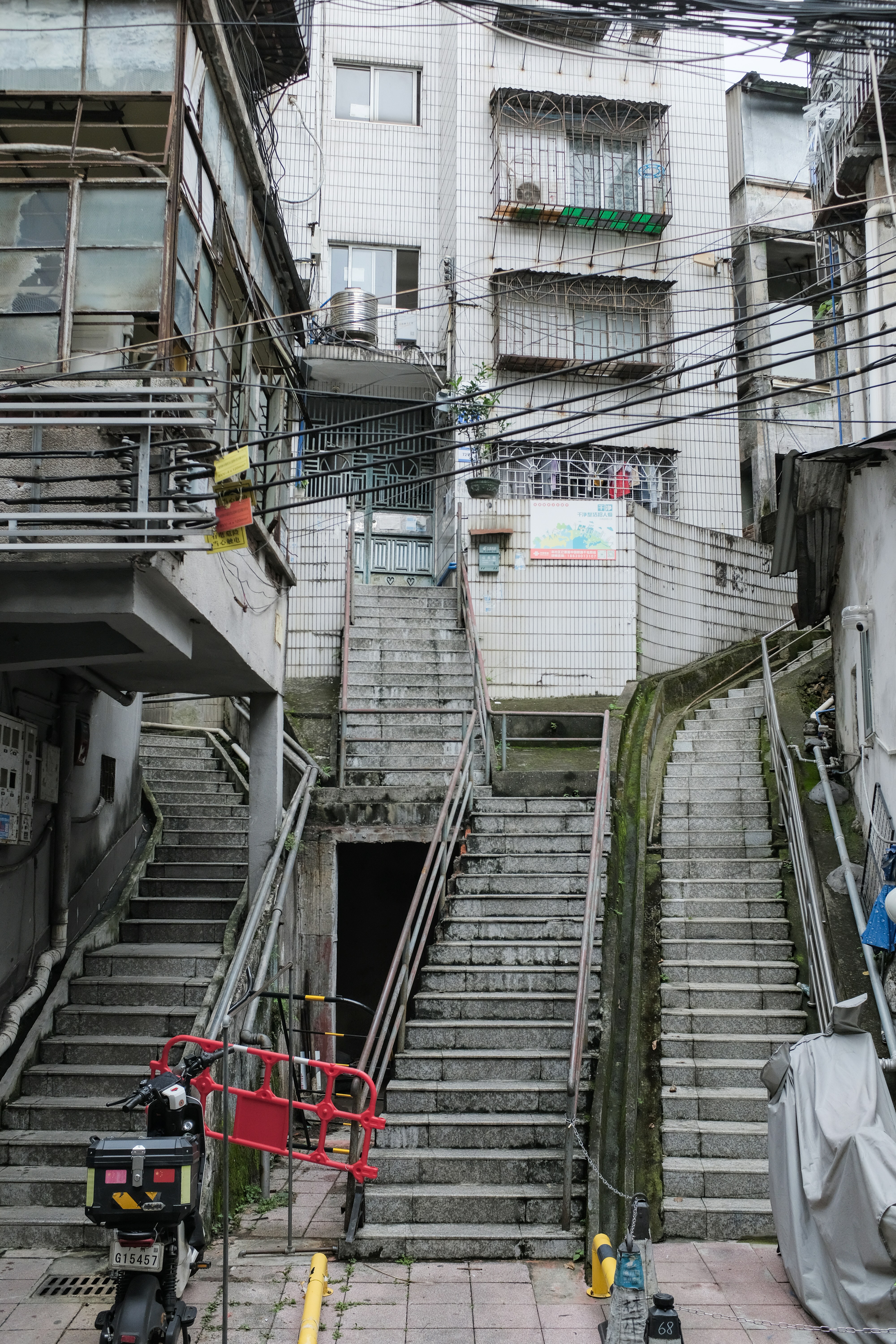 Concrete stairs ascend between aged buildings with wires.