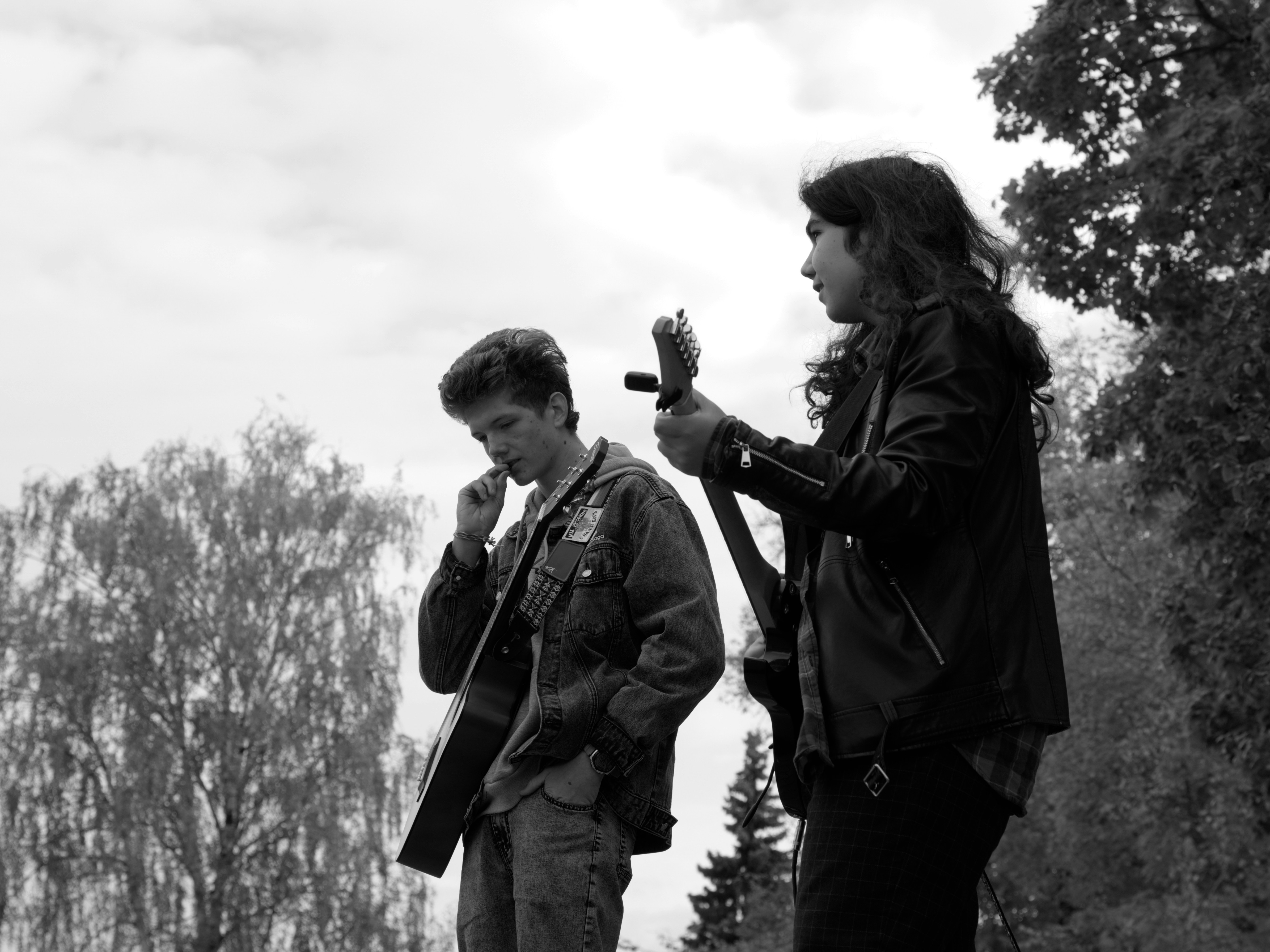 Two people stand outdoors with trees behind them.