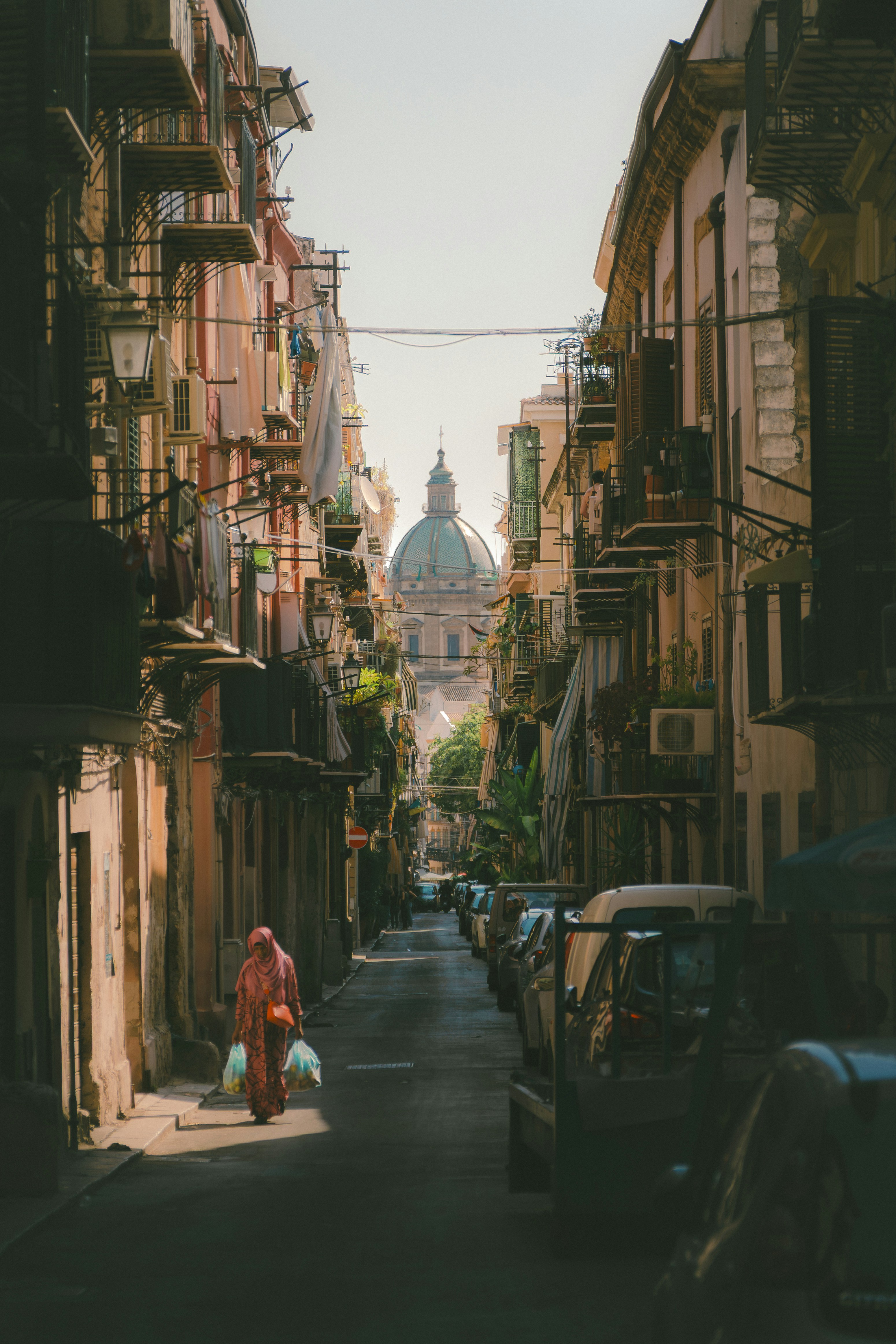 A person walks down a narrow street towards a dome.