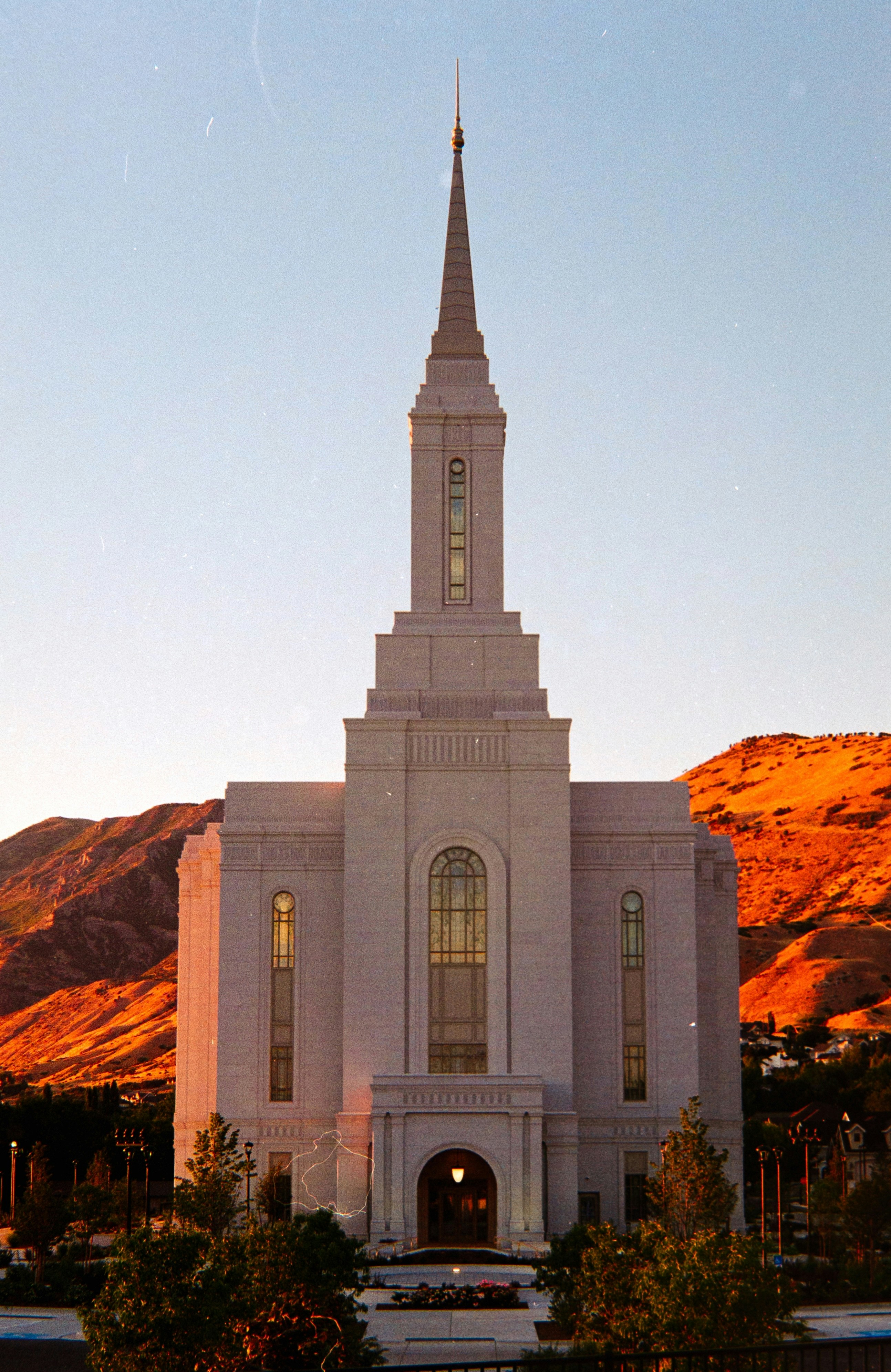 Templo branco com pináculo contra montanhas alaranjadas ao pôr do sol.